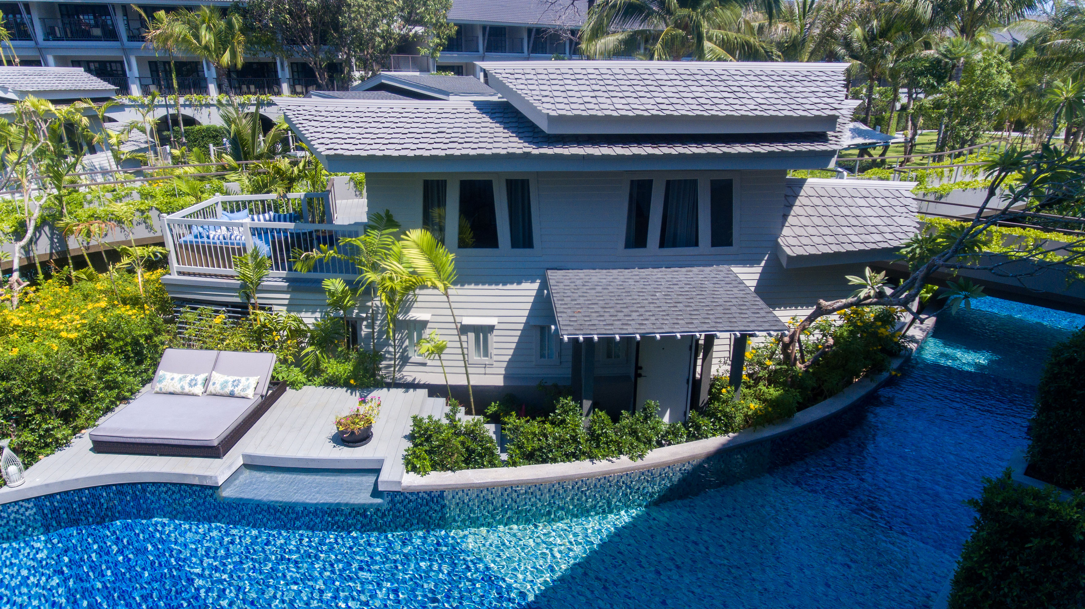 Tropical resort villa with blue swimming pool, sun deck, and lush greenery.