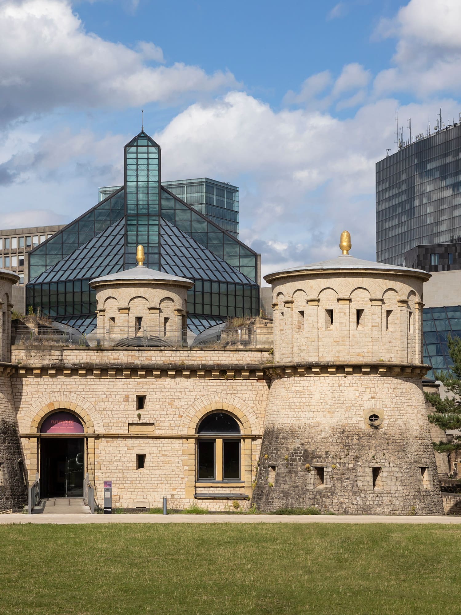 a stone building with towers and a green lawn in front of a city