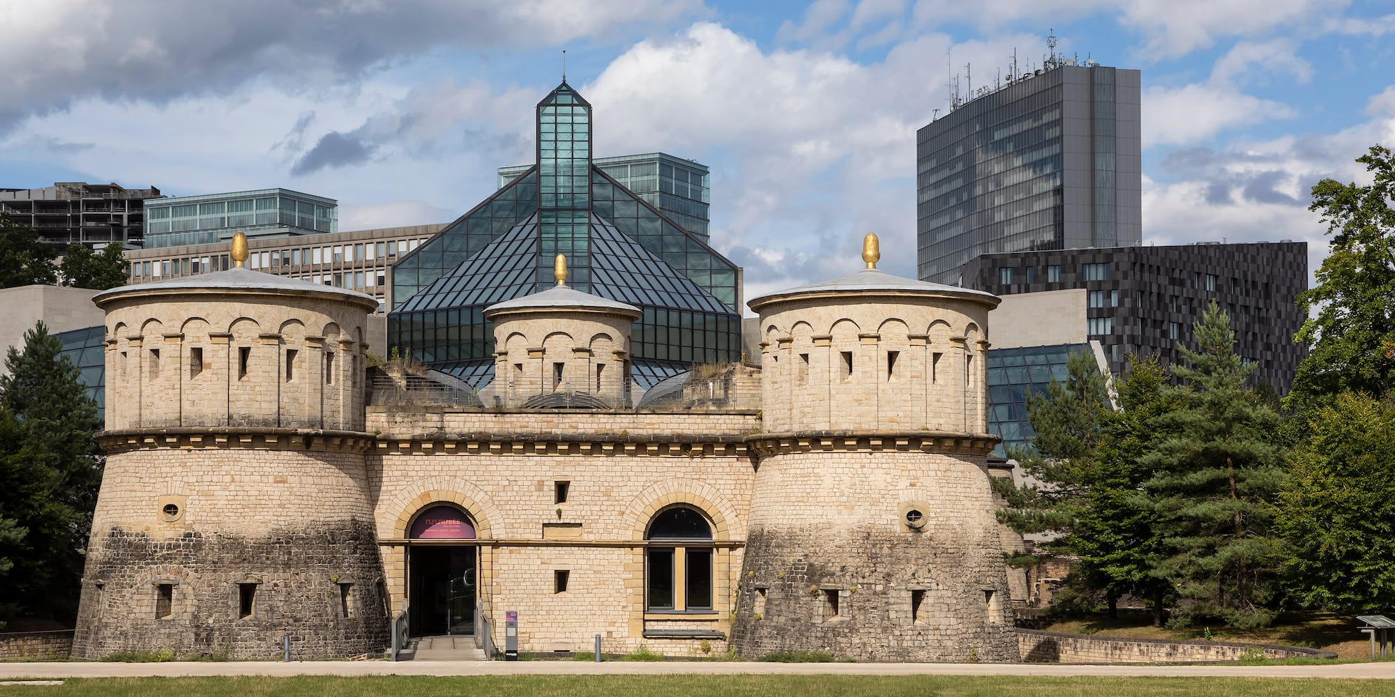 a stone building with towers and a green lawn in front of a city