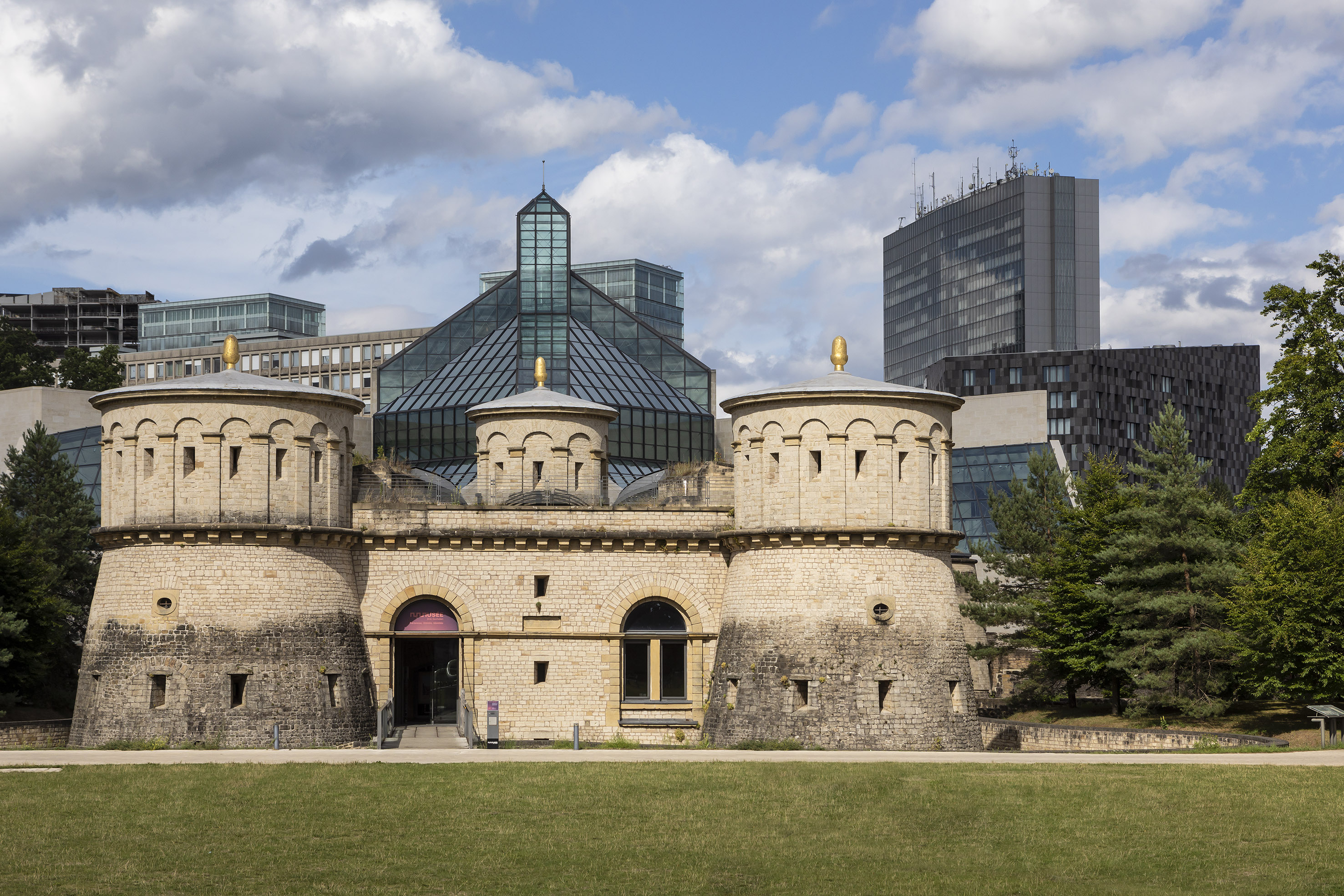a stone building with towers and a green lawn in front of a city