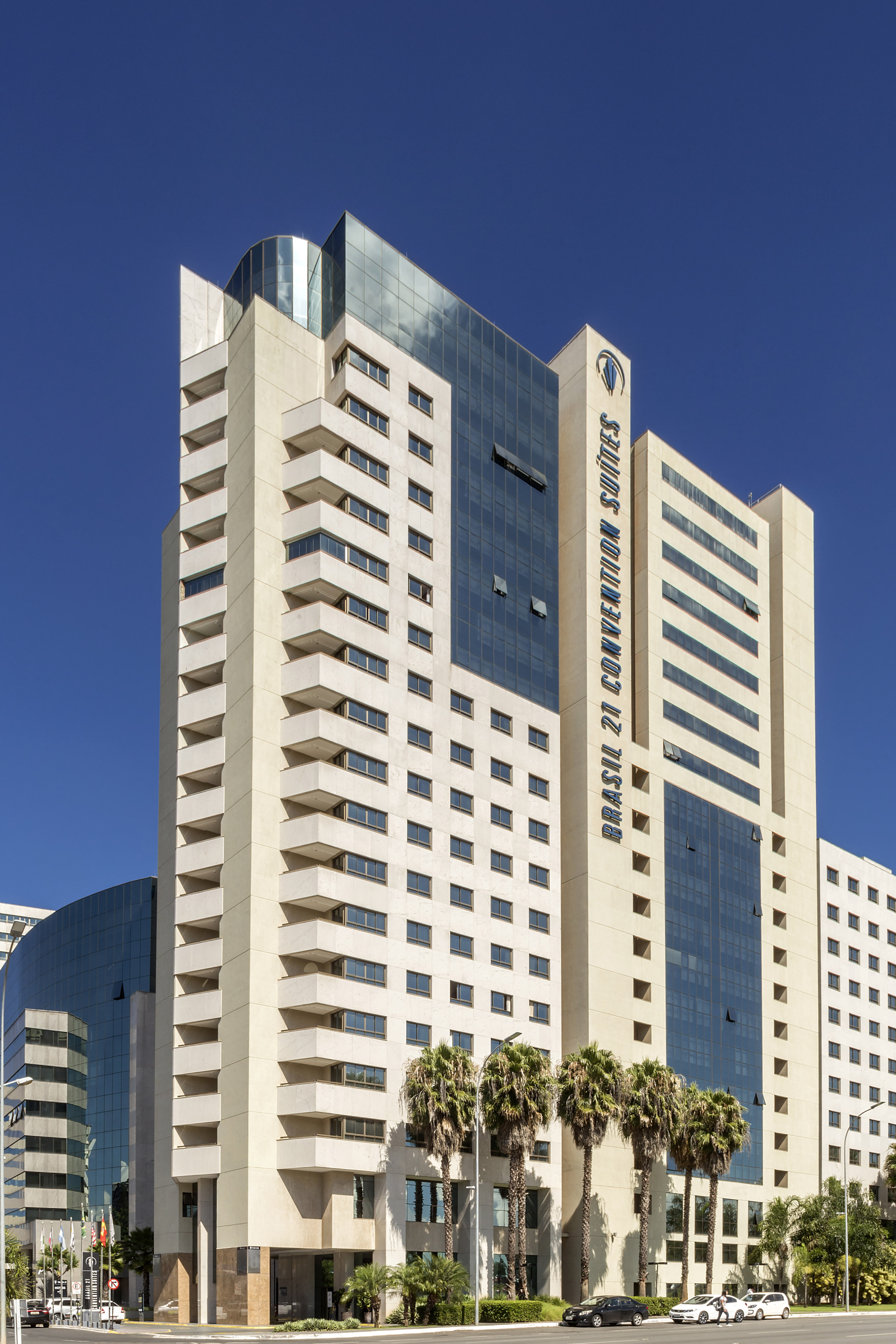 Modern Brasil 21 Convention Suites hotel exterior with blue glass and palm trees.