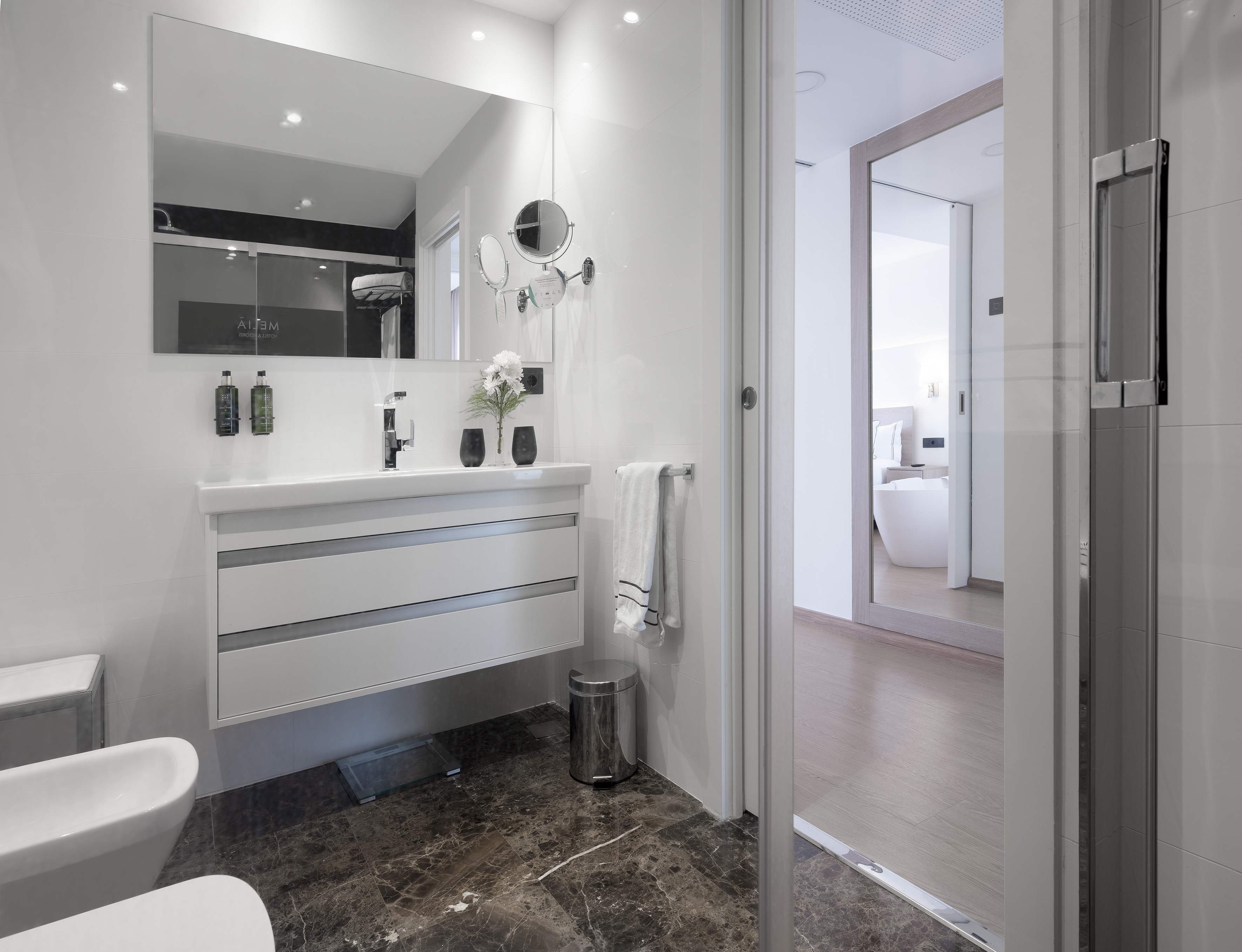 Modern hotel bathroom with white vanity, dark marble floor, glass shower.