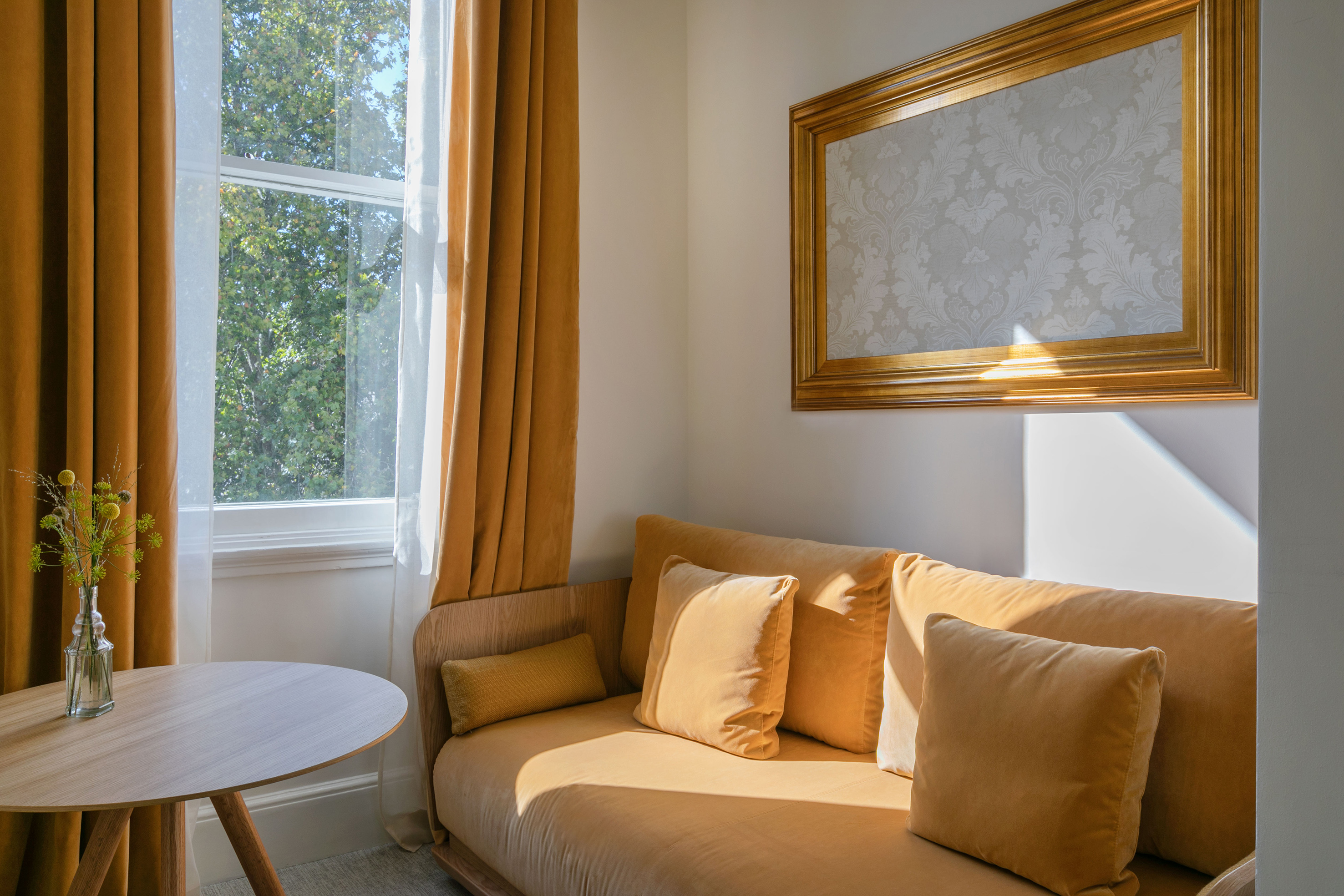Cozy room with golden velvet sofa, matching curtains, wooden table, sunny window.
