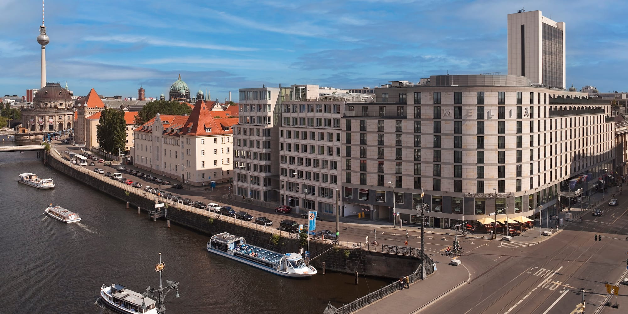 Berlin Spree River cityscape with boats, TV Tower, and diverse architecture.