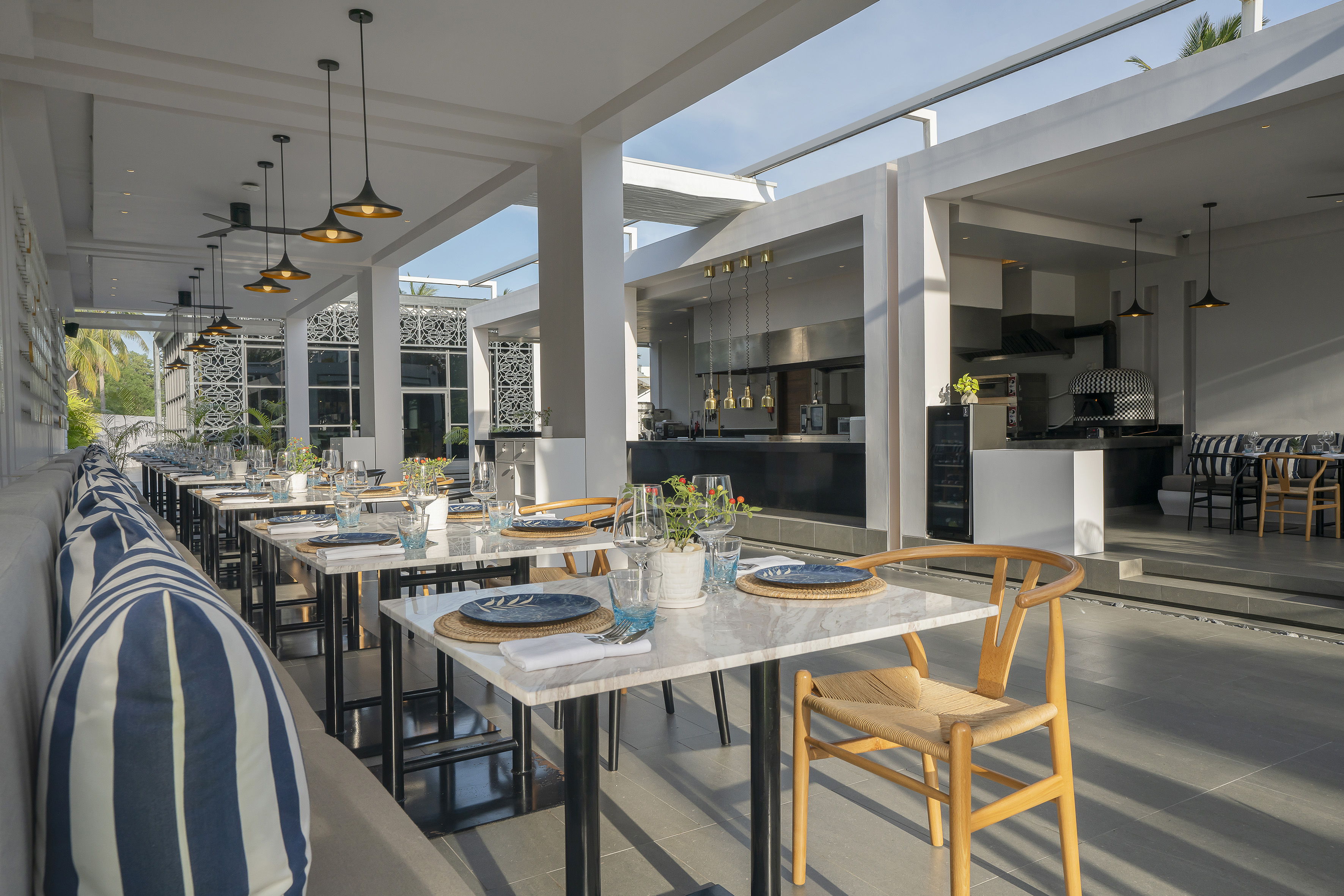 Modern open-air restaurant with set tables, striped banquette, and open kitchen.