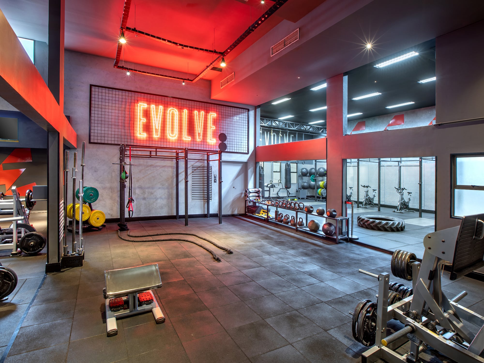Modern gym with 'EVOLVE' neon sign, weights, and diverse workout equipment.