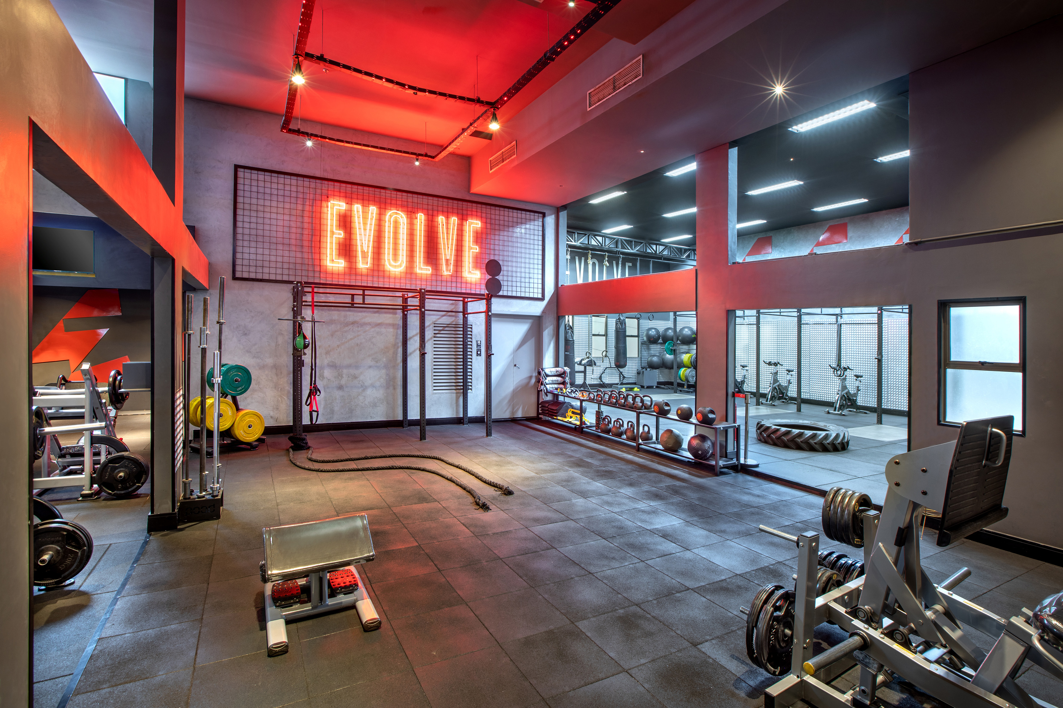 Modern gym with 'EVOLVE' neon sign, weights, and diverse workout equipment.