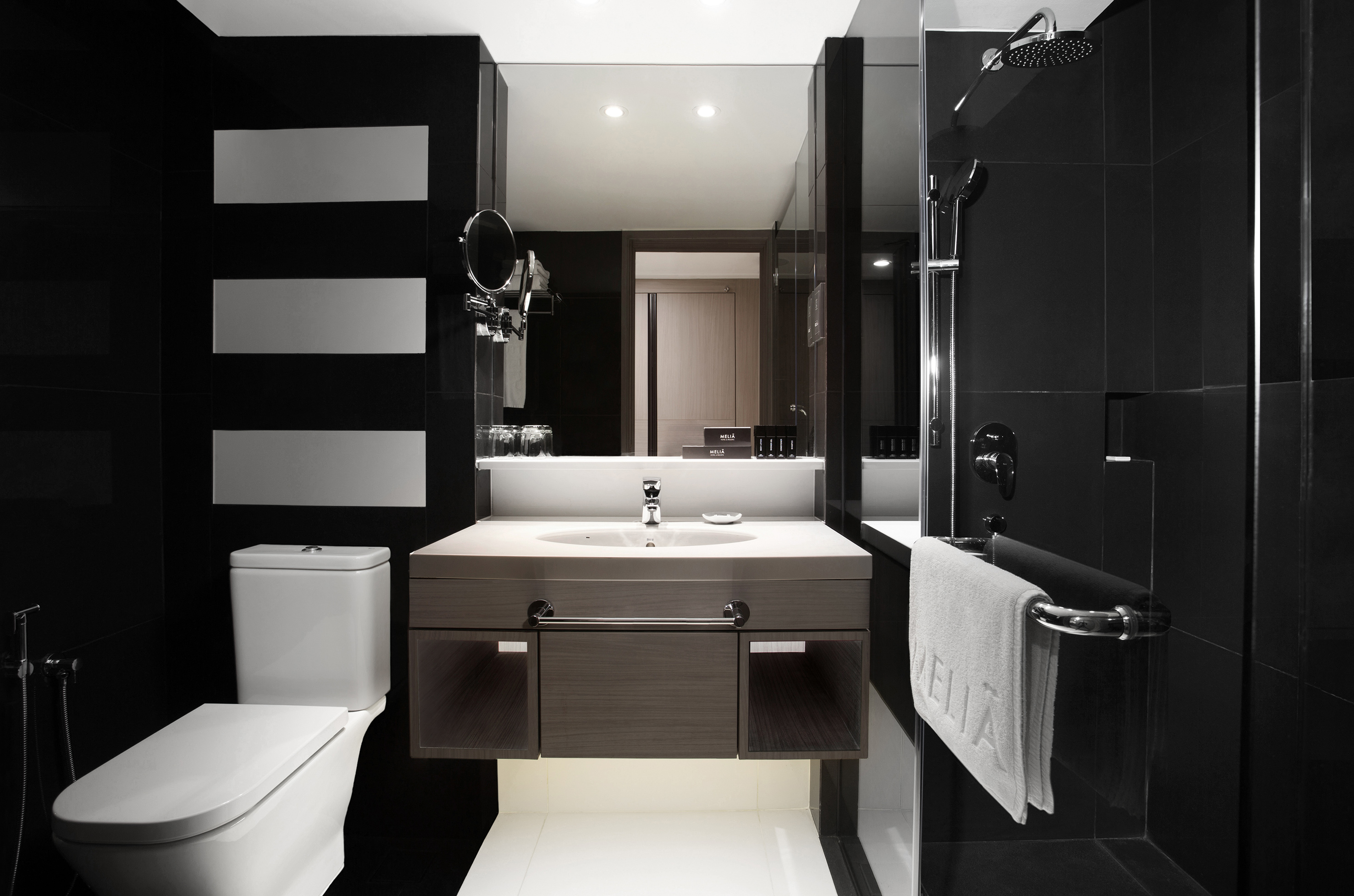 Modern black hotel bathroom with toilet, vanity, and walk-in shower.