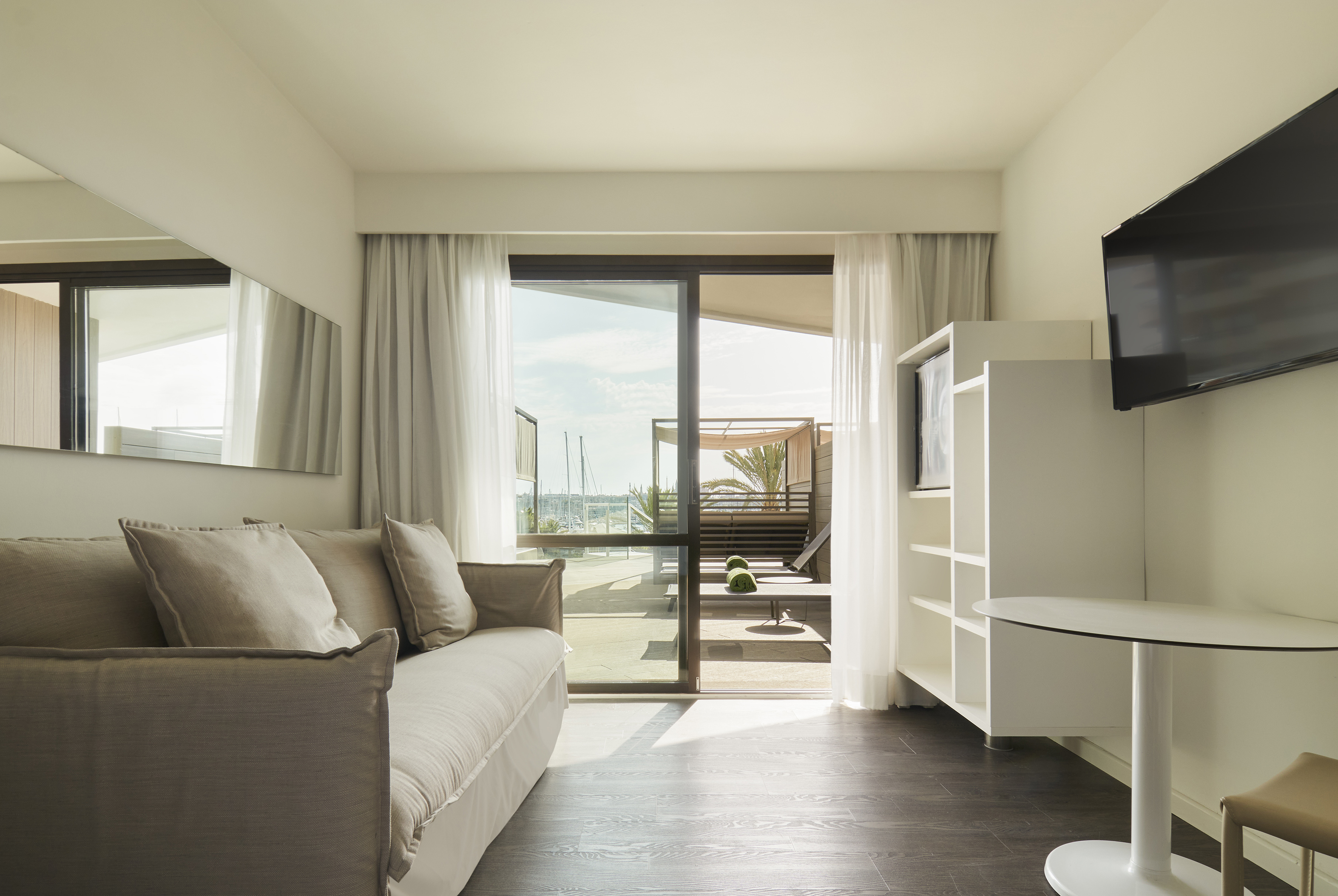 Modern hotel suite living room with marina view patio, sofa, and TV.