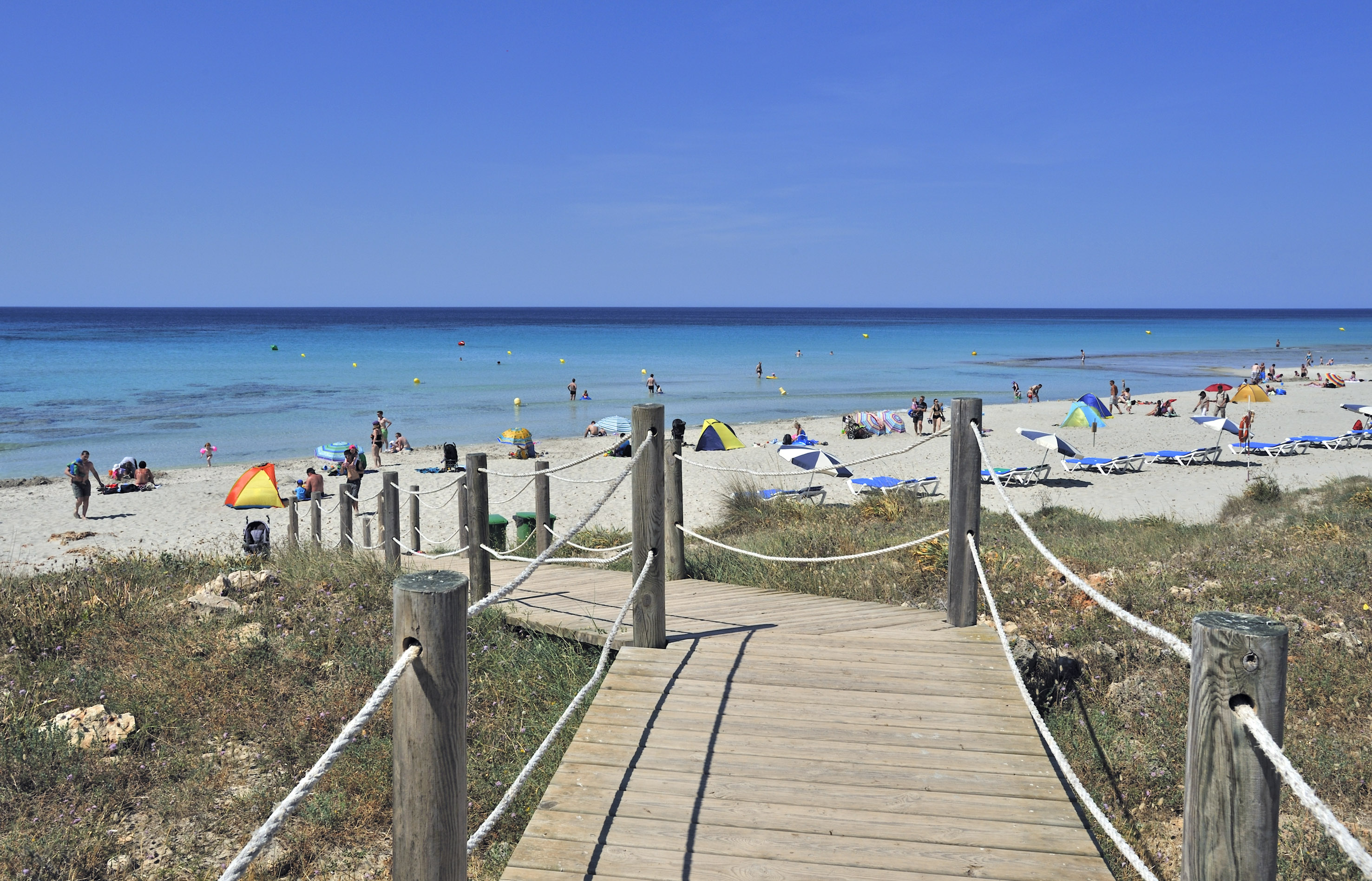 Wooden boardwalk leading to a sunny sandy beach with turquoise ocean and people.