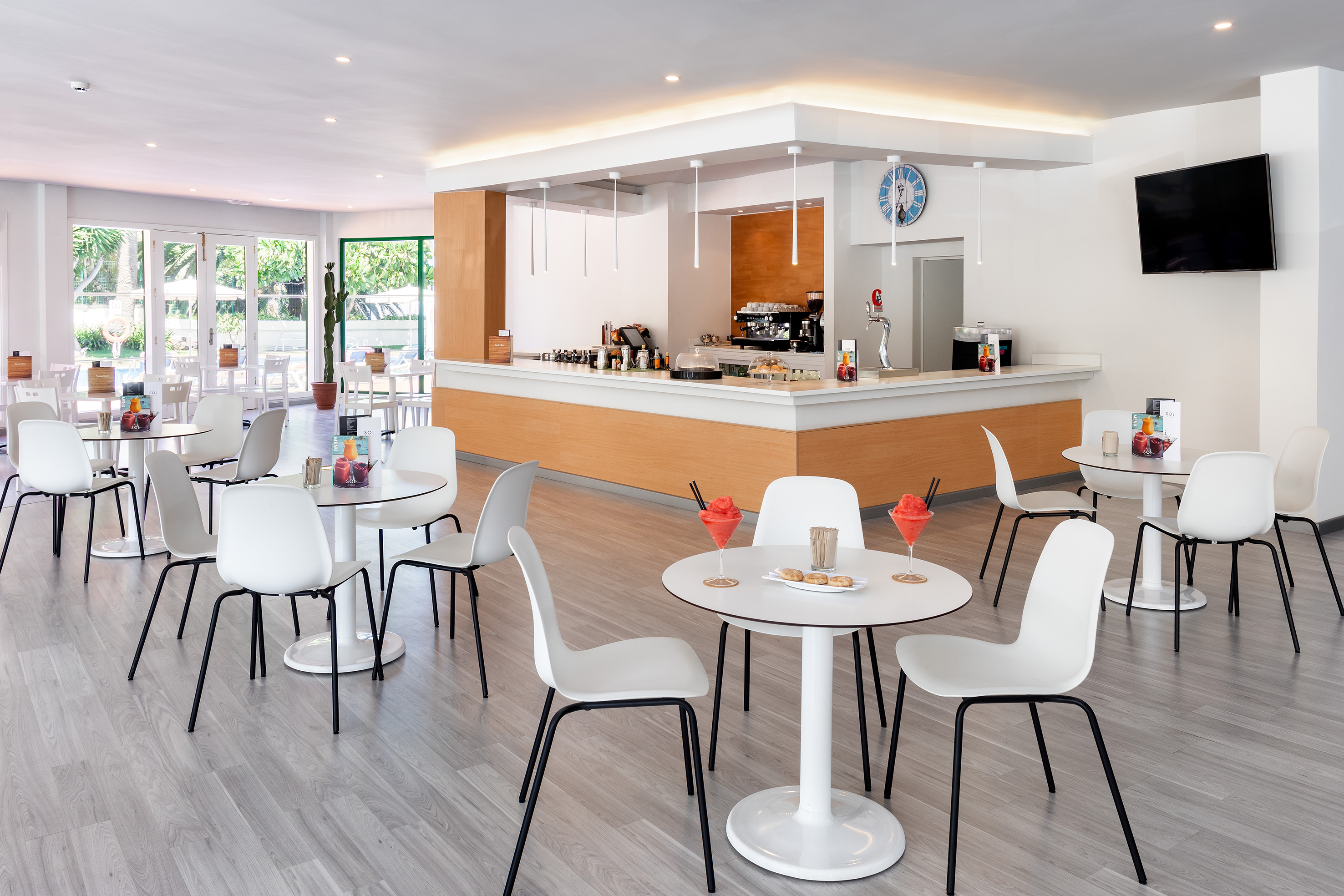 Bright modern cafe bar with white tables, wooden counter, and outdoor views.