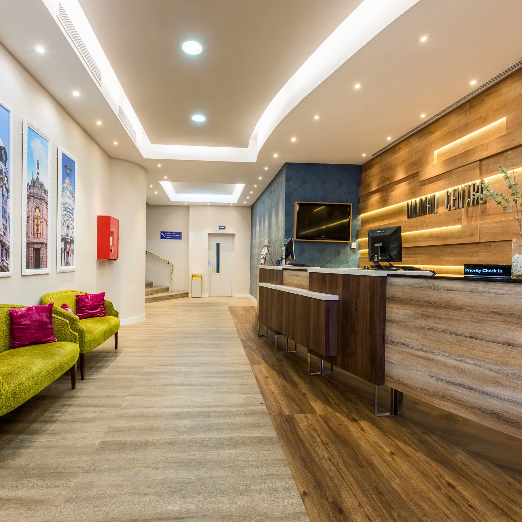 Modern hotel lobby with wood reception desk, green seating, and city artwork.