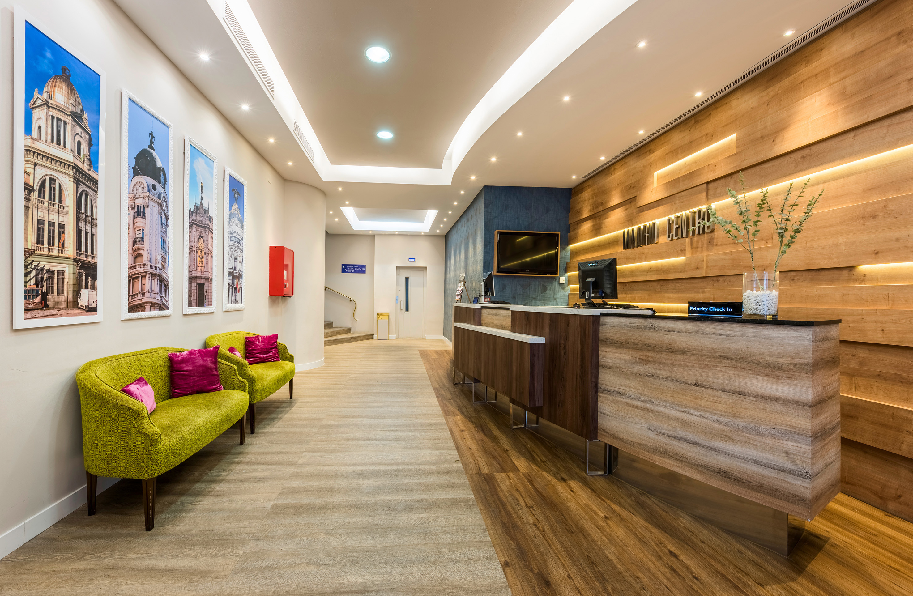 Modern hotel lobby with wood reception desk, green seating, and city artwork.