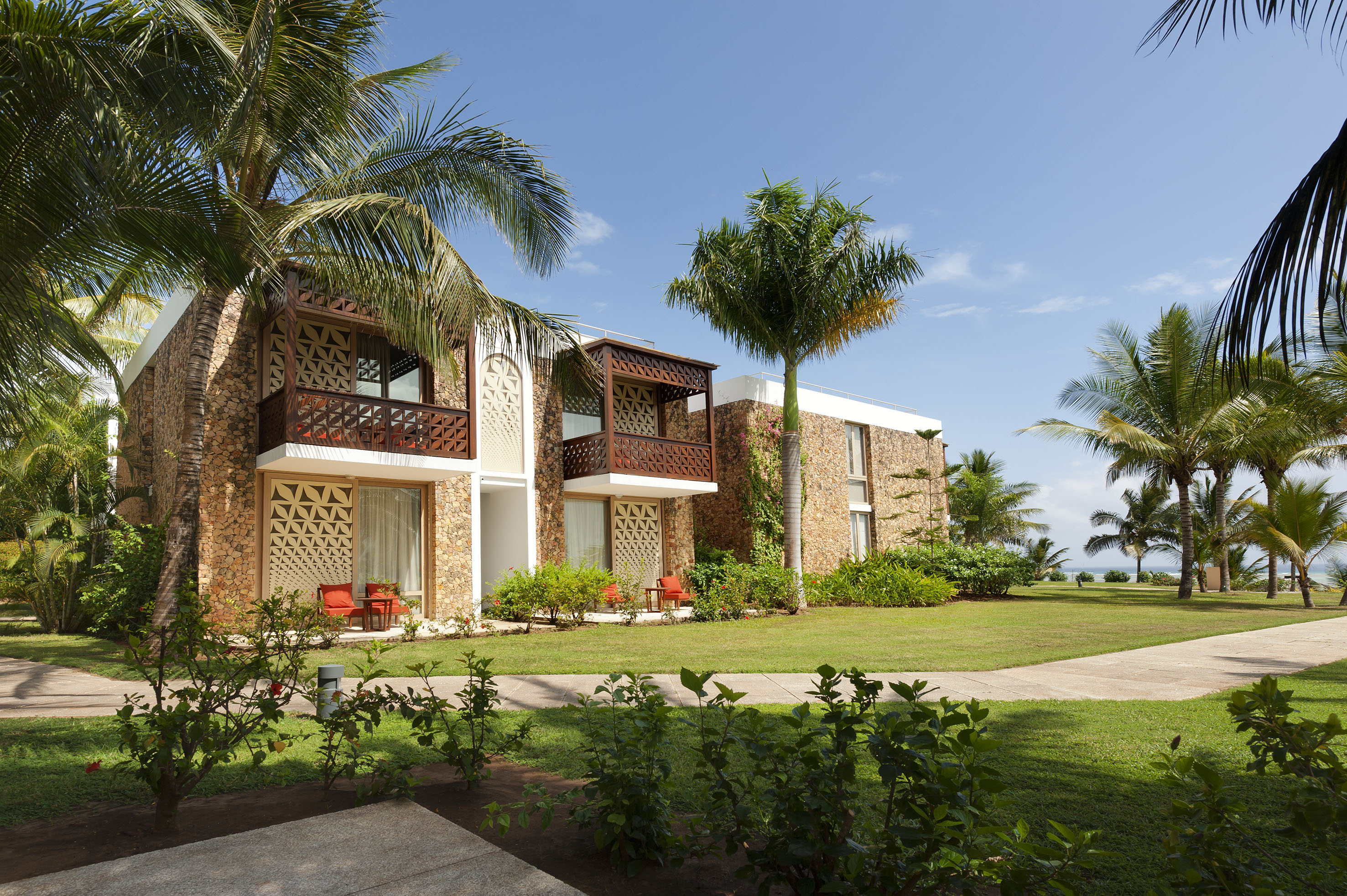 Tropical resort building with stone facade, wooden balconies, palm trees, lush garden.