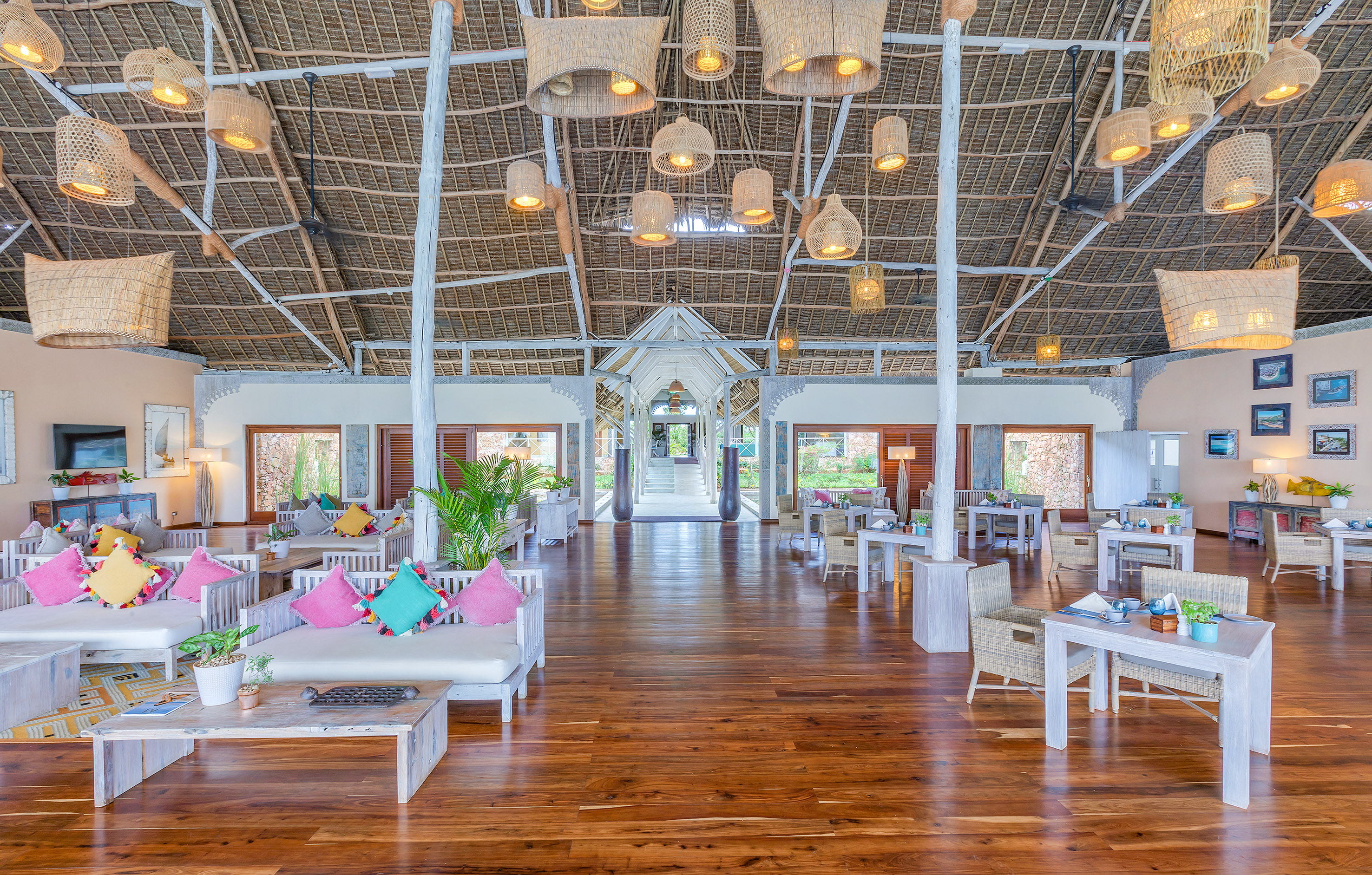 Tropical resort lounge with thatched roof, wood floor, and woven pendant lights.