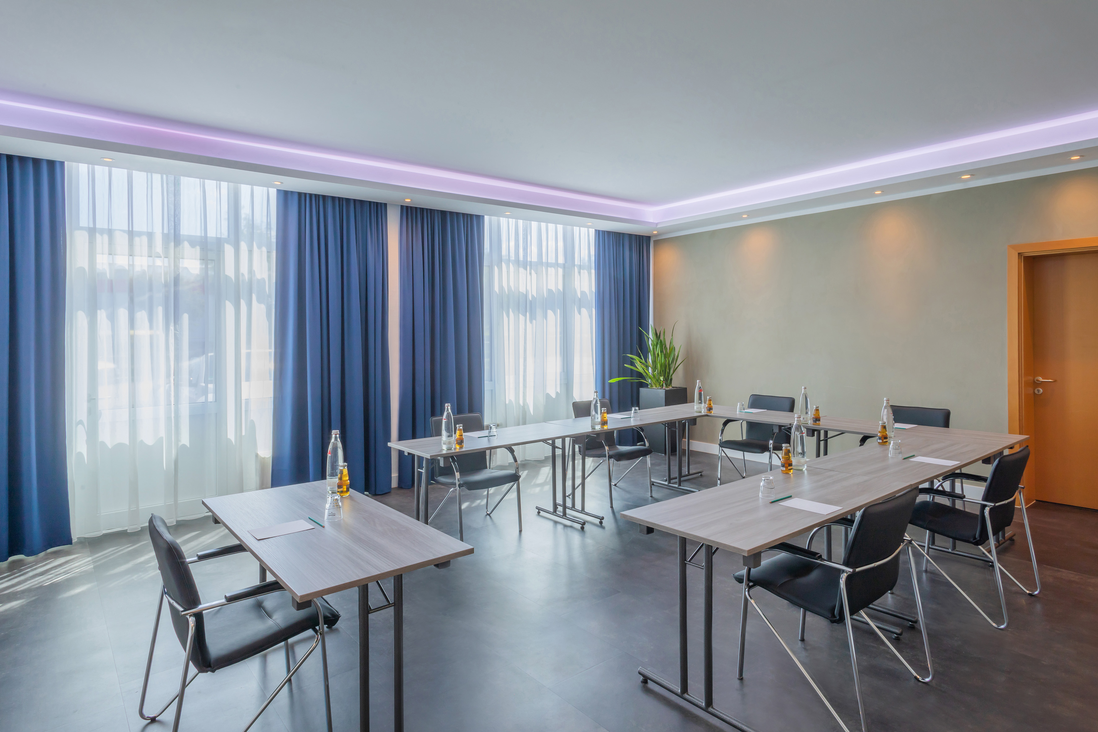 Modern meeting room with U-shaped table setup, black chairs, and blue curtains.