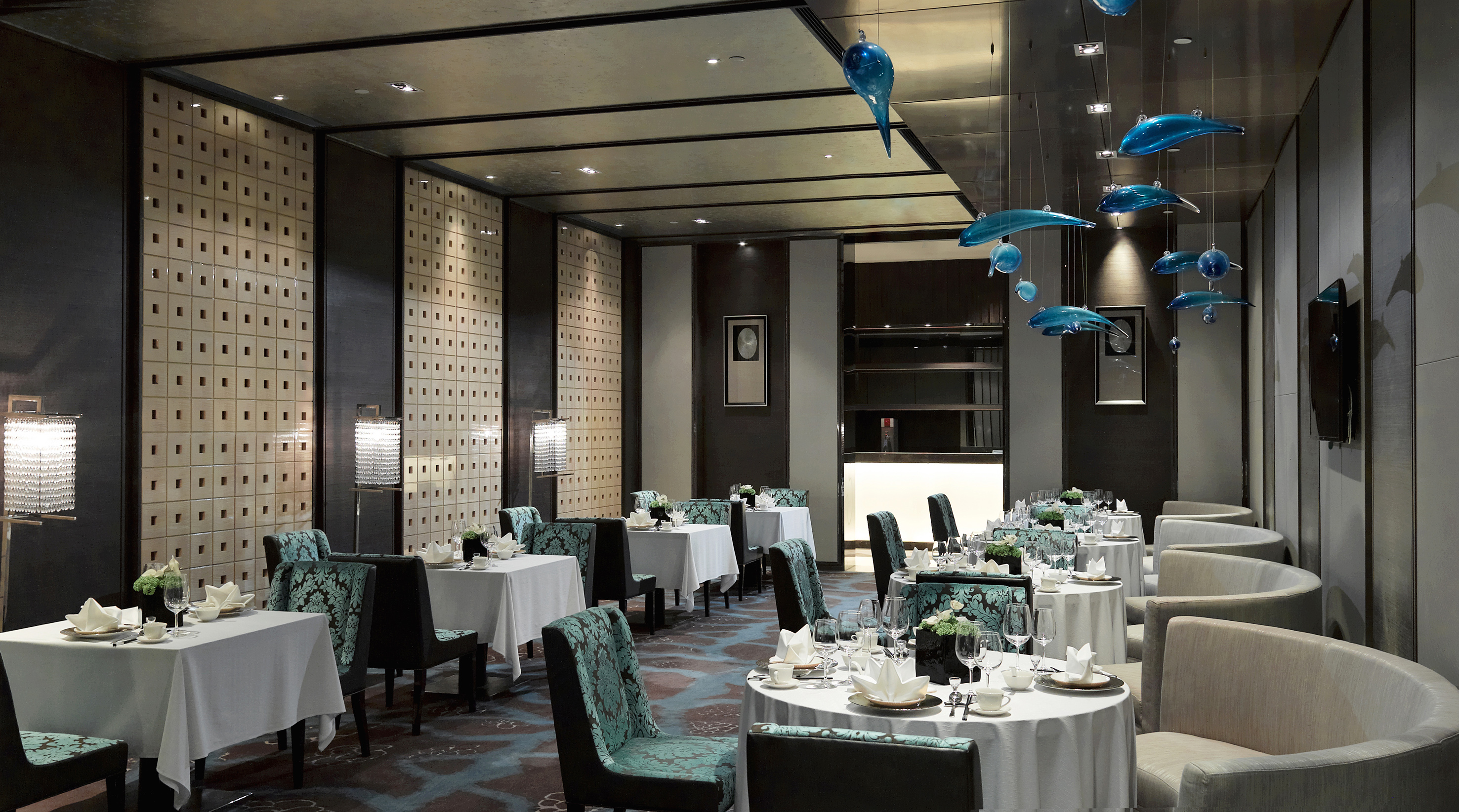Elegant luxury restaurant dining room with blue glass fish sculptures and set tables.