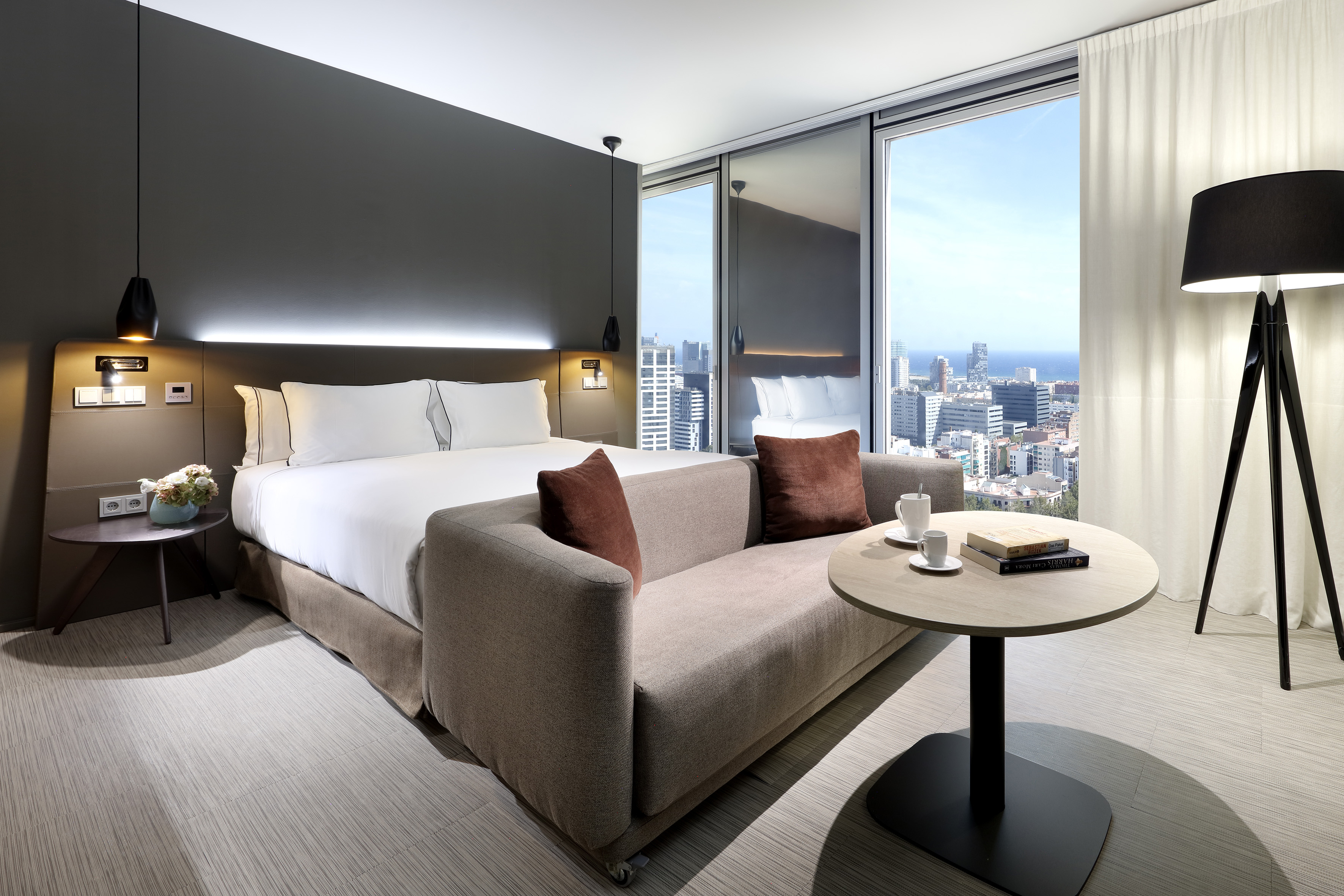 Modern hotel room with bed, sofa, and expansive city/ocean view.