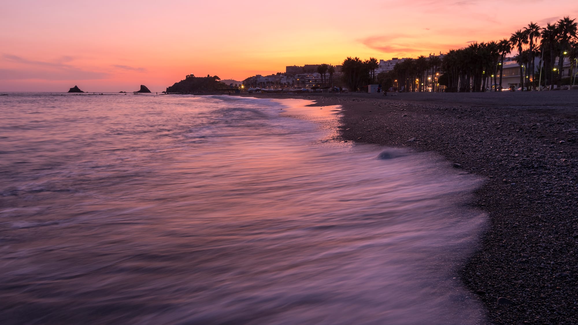 a beach with a body of water and buildings in the background