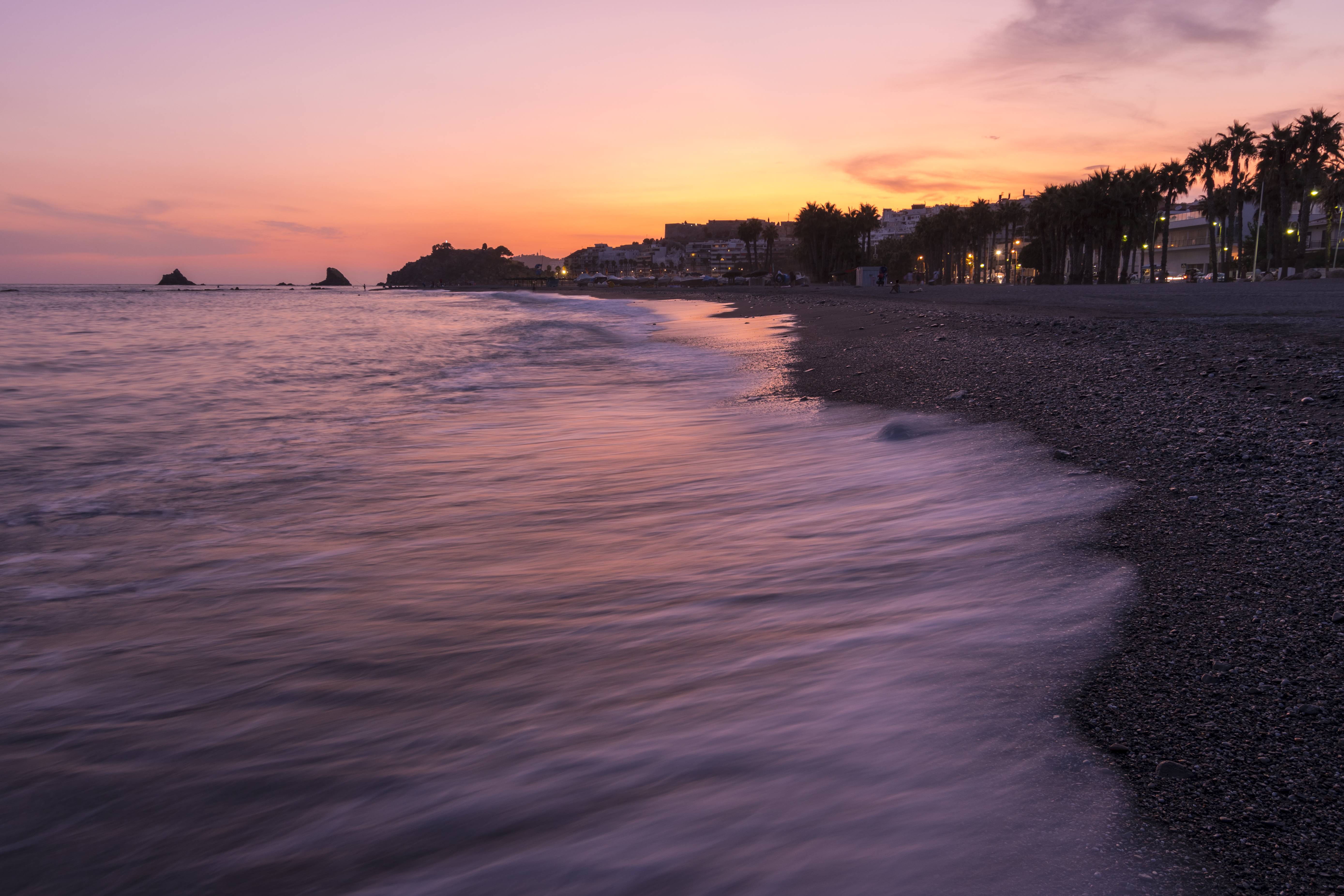 a beach with a body of water and buildings in the background