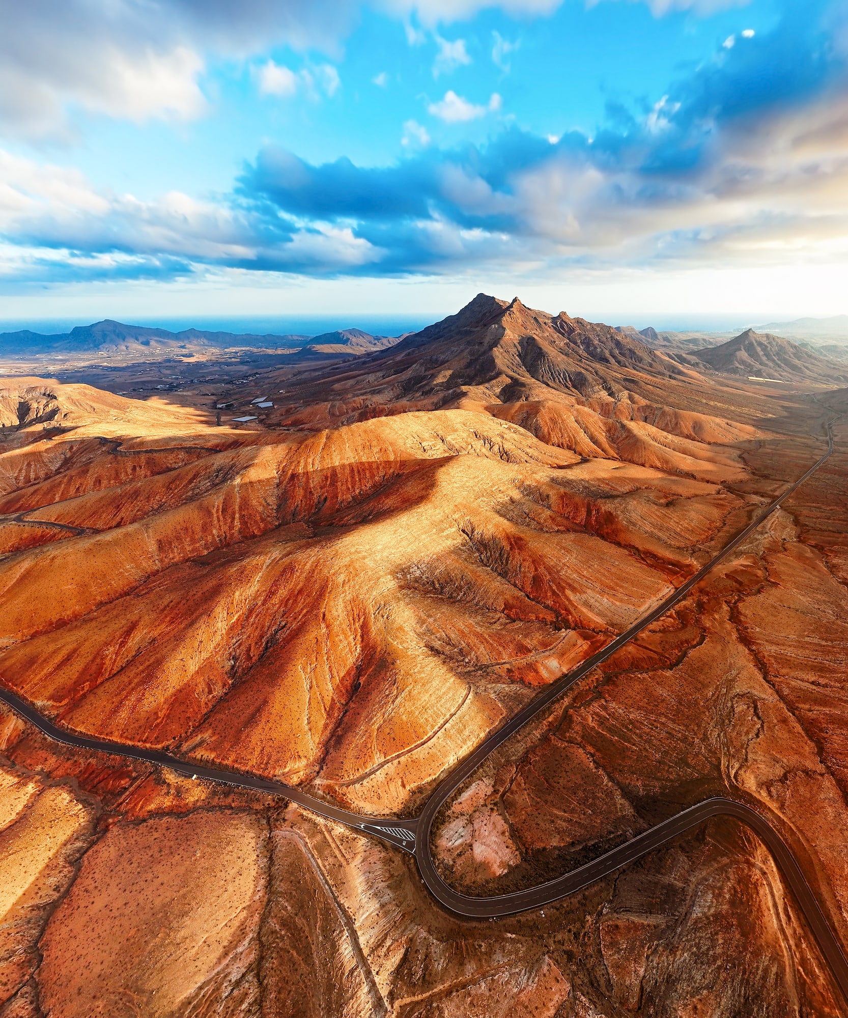 Aerial Fuerteventura mountain landscape with winding road and distant ocean view.