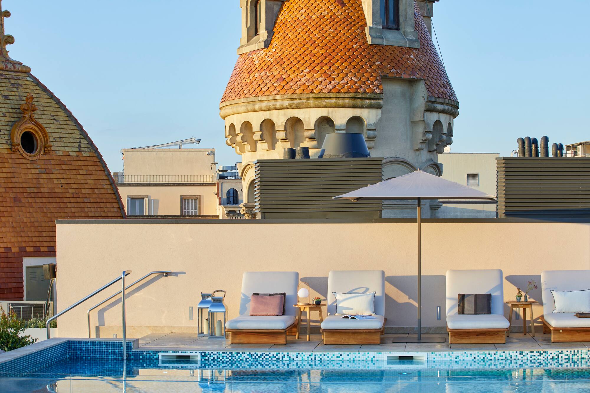 Rooftop hotel pool with lounge chairs, umbrella, and historic tiled tower.