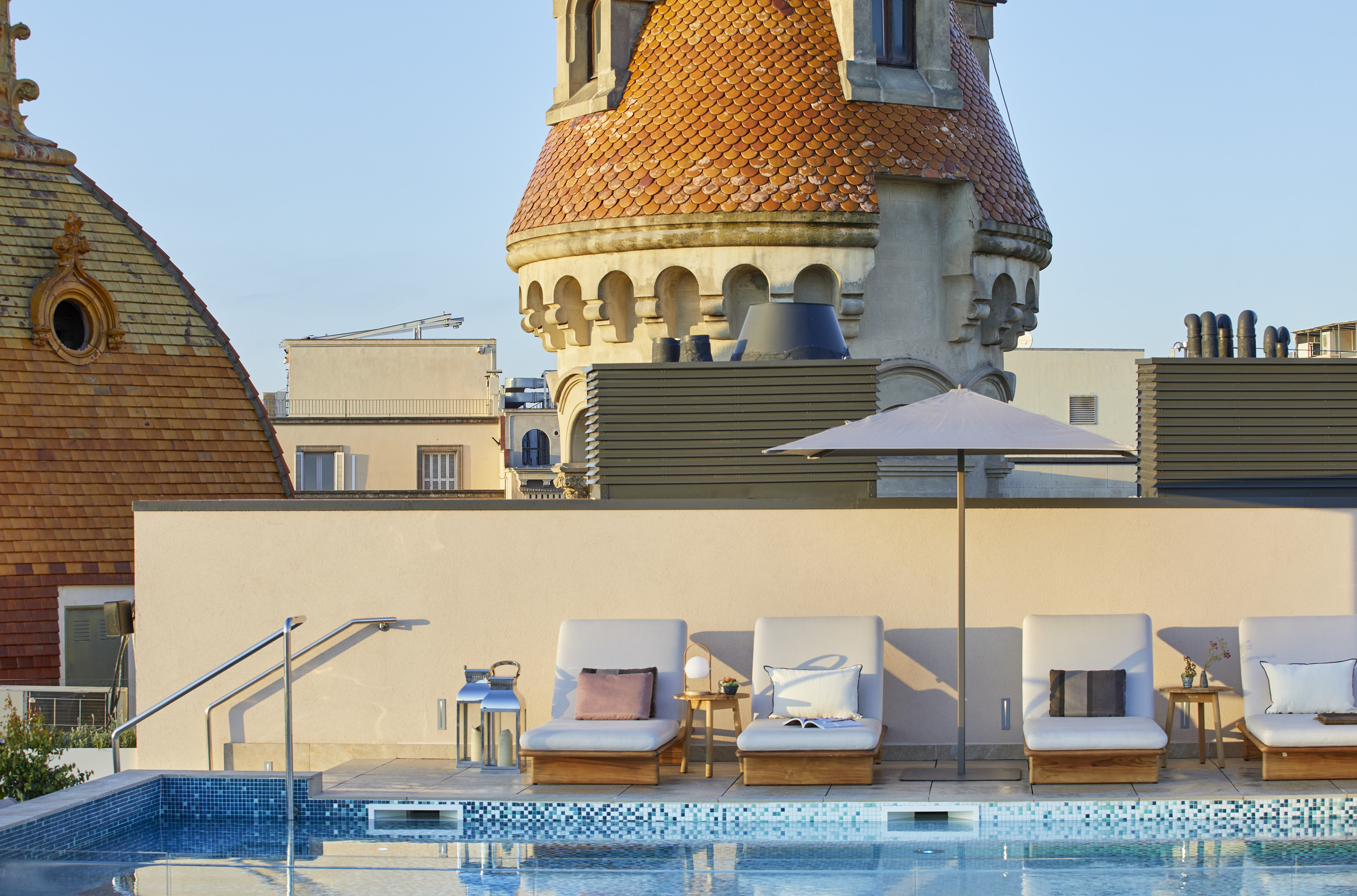 Rooftop hotel pool with lounge chairs, umbrella, and historic tiled tower.