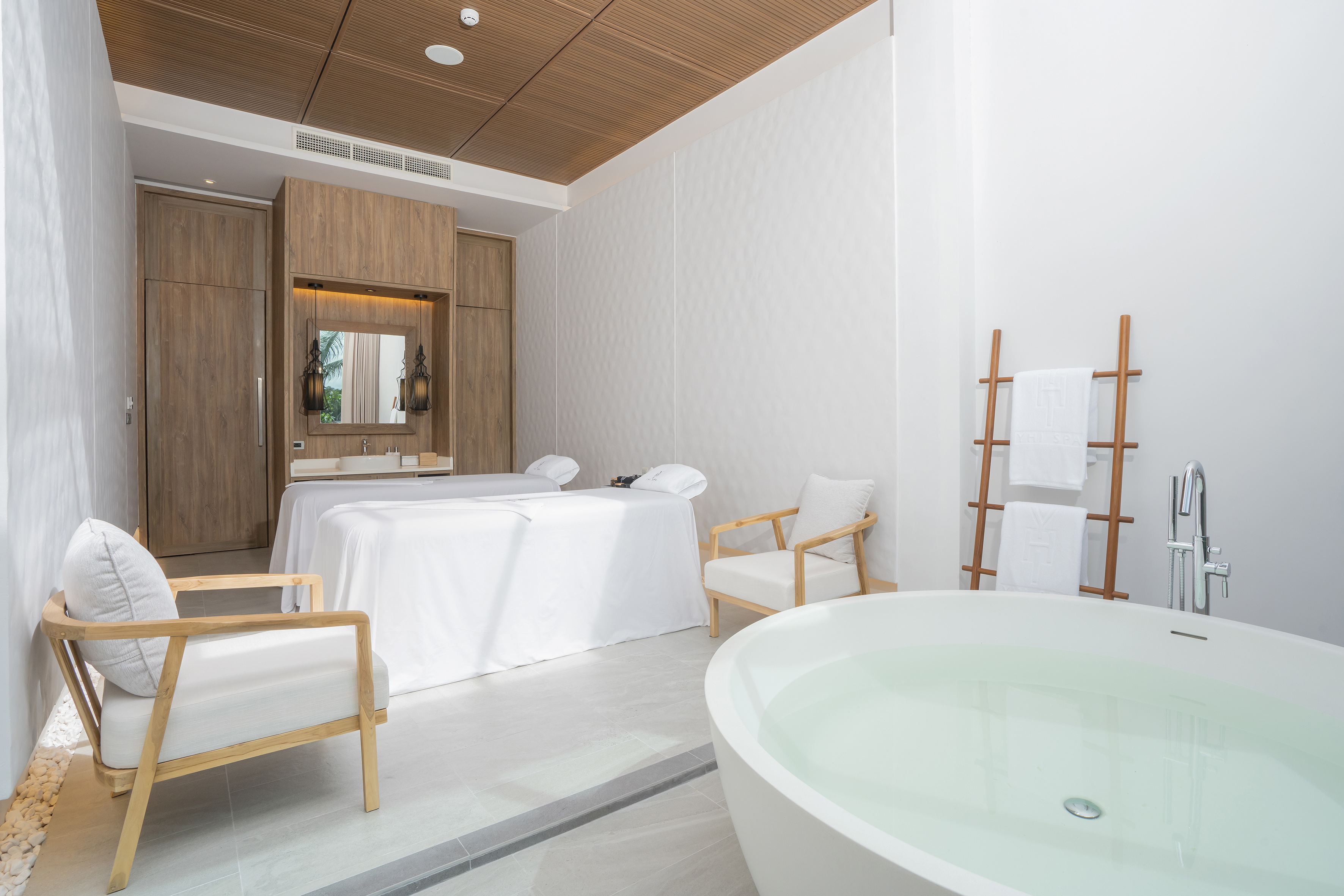 Bright spa room with dual massage beds, soaking tub, and wooden ceiling.