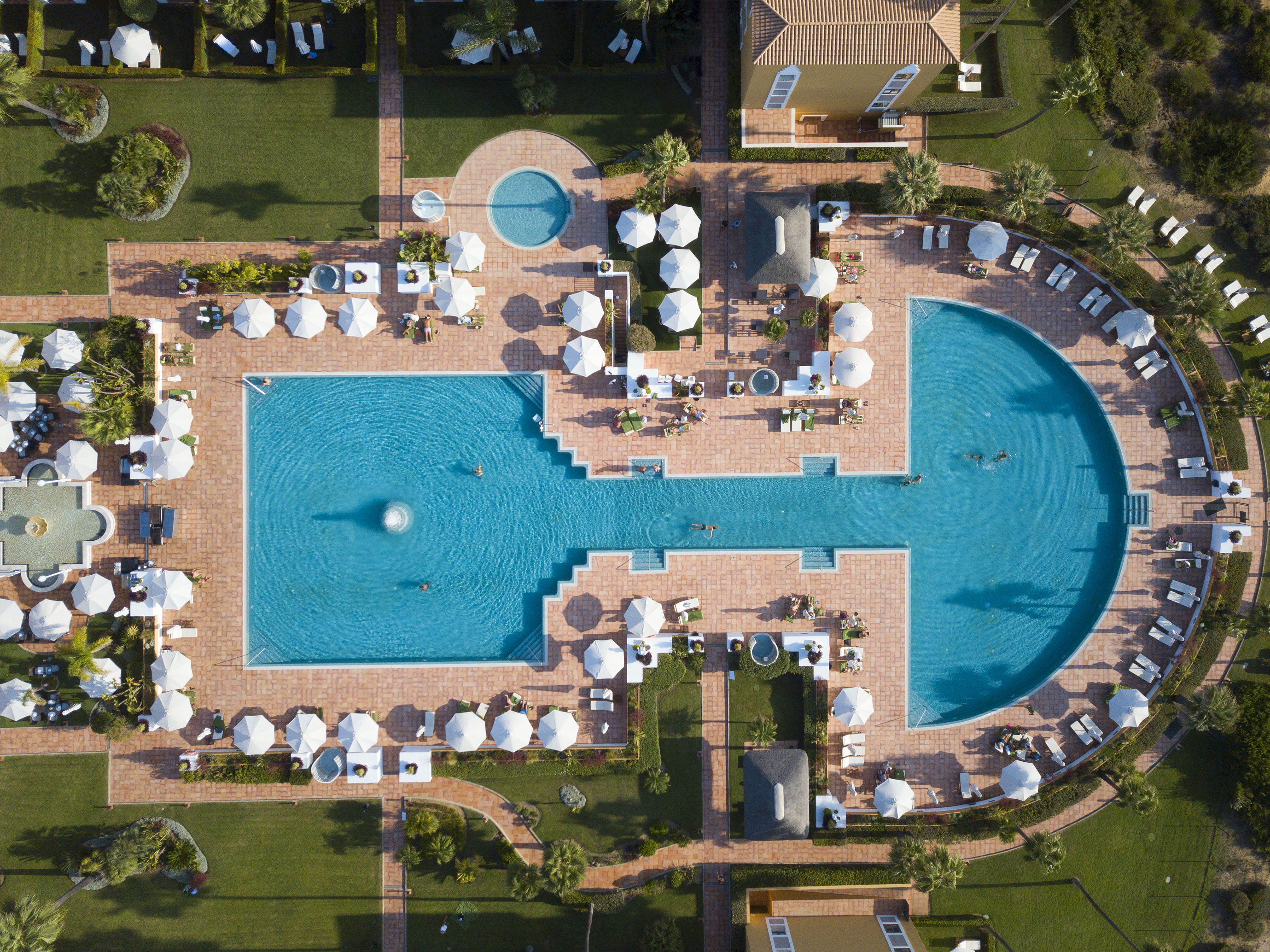 Aerial view: Resort with large blue pools, white umbrellas, and sun loungers.