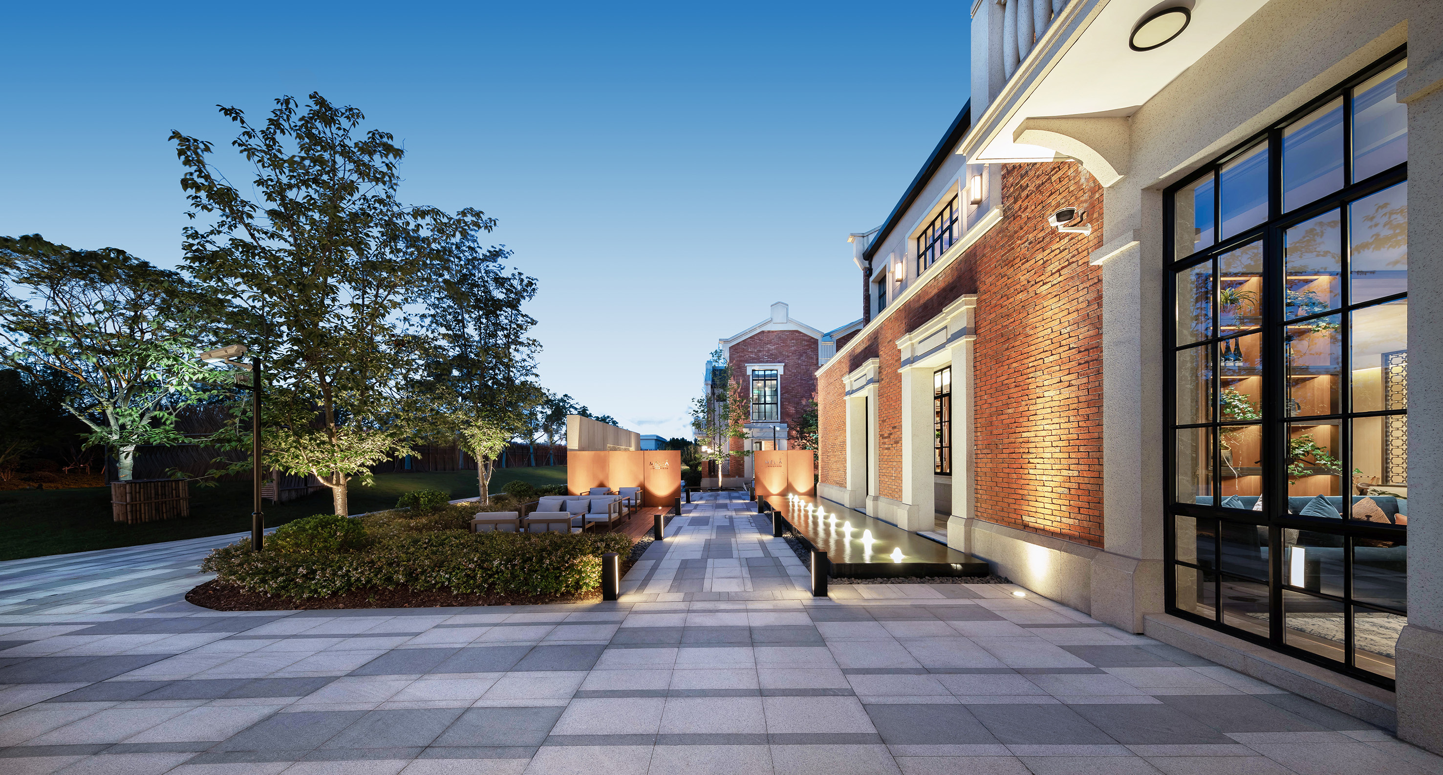 Modern brick courtyard, outdoor seating, water feature, and evening lighting.