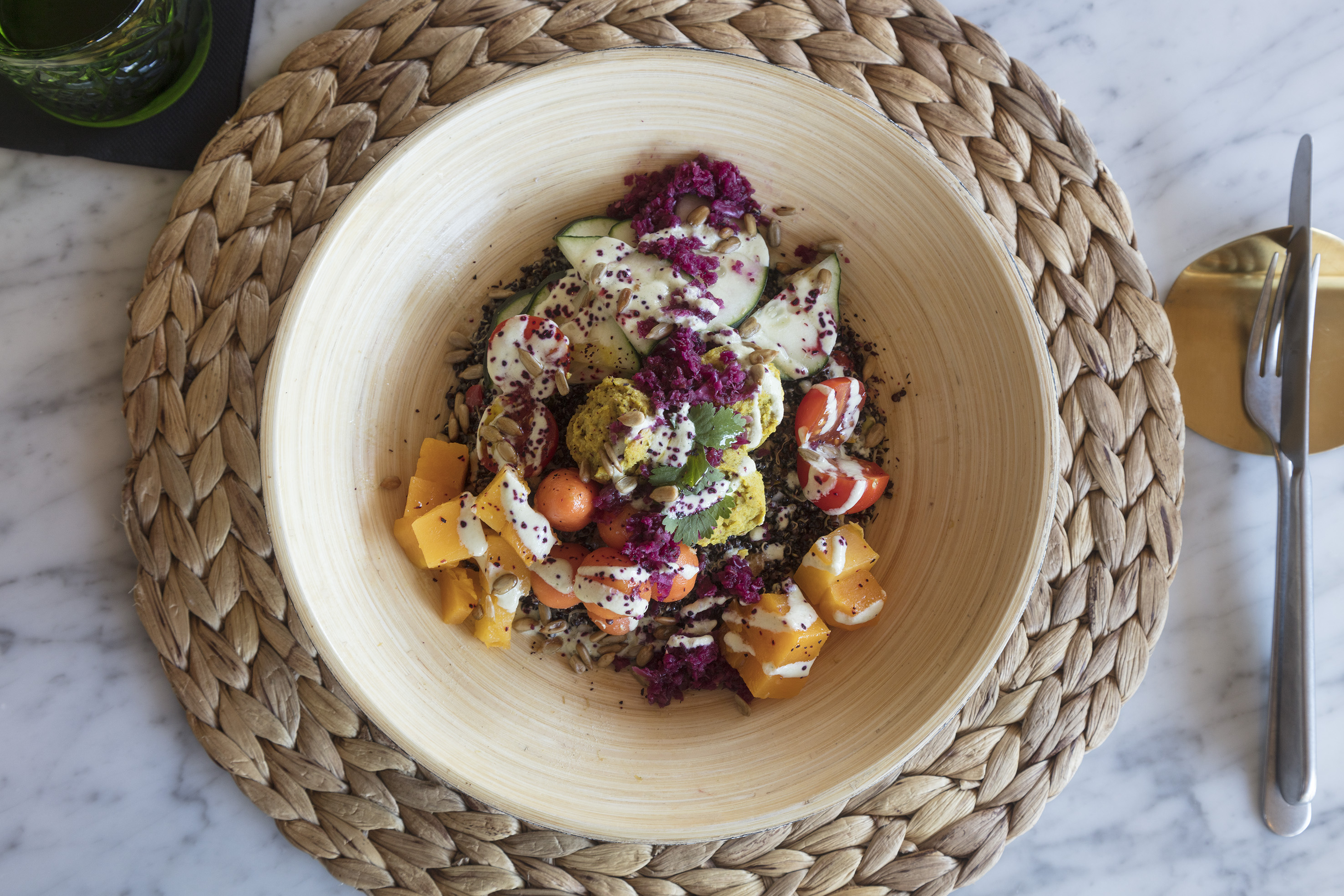 Colorful buddha bowl with squash, zucchini, red cabbage, seeds, and dressing.