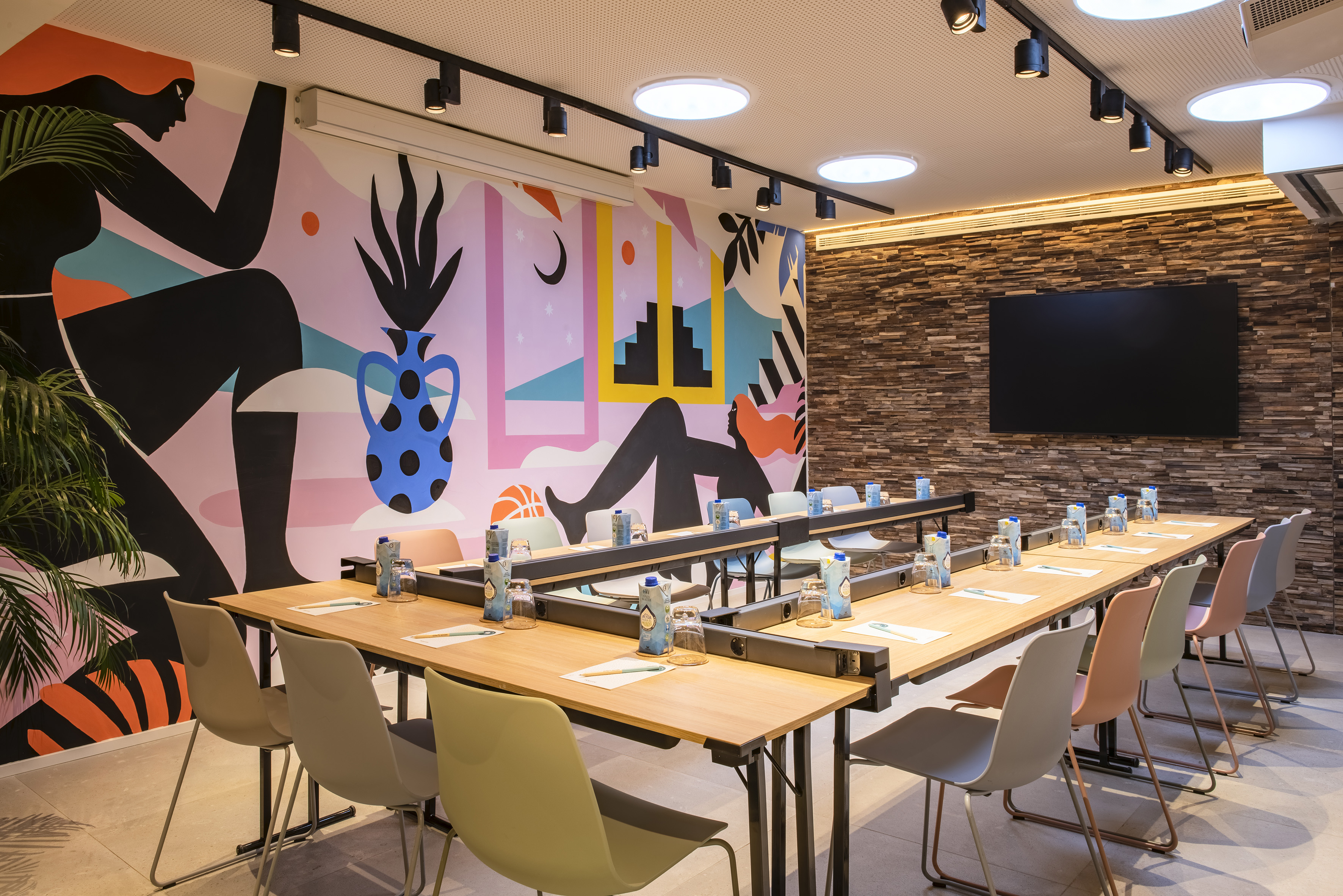 Modern conference room with vibrant mural, U-shaped tables, and large screen.