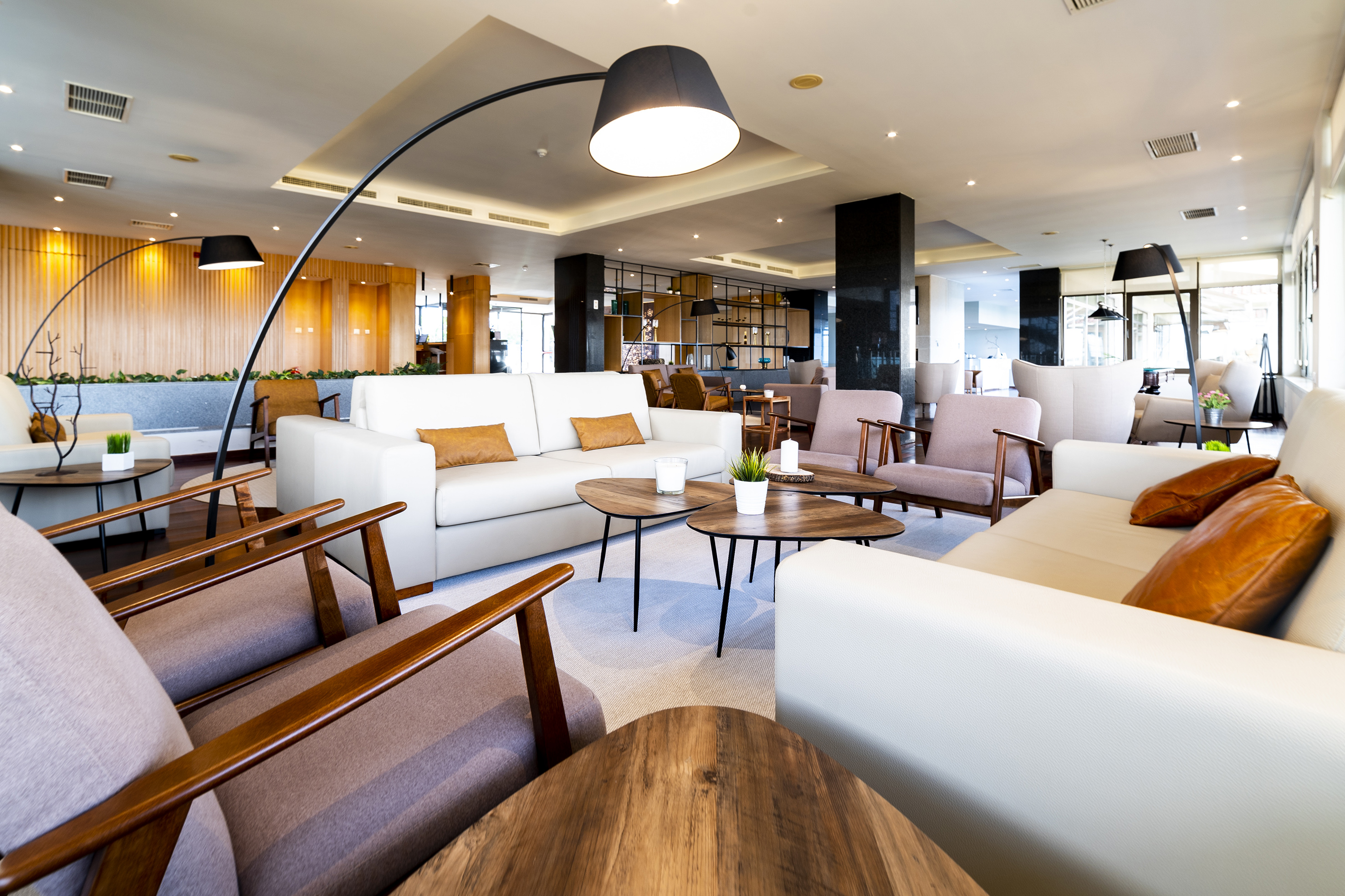 Modern hotel lobby with white sofas, armchairs, wood tables, and arc lamp.