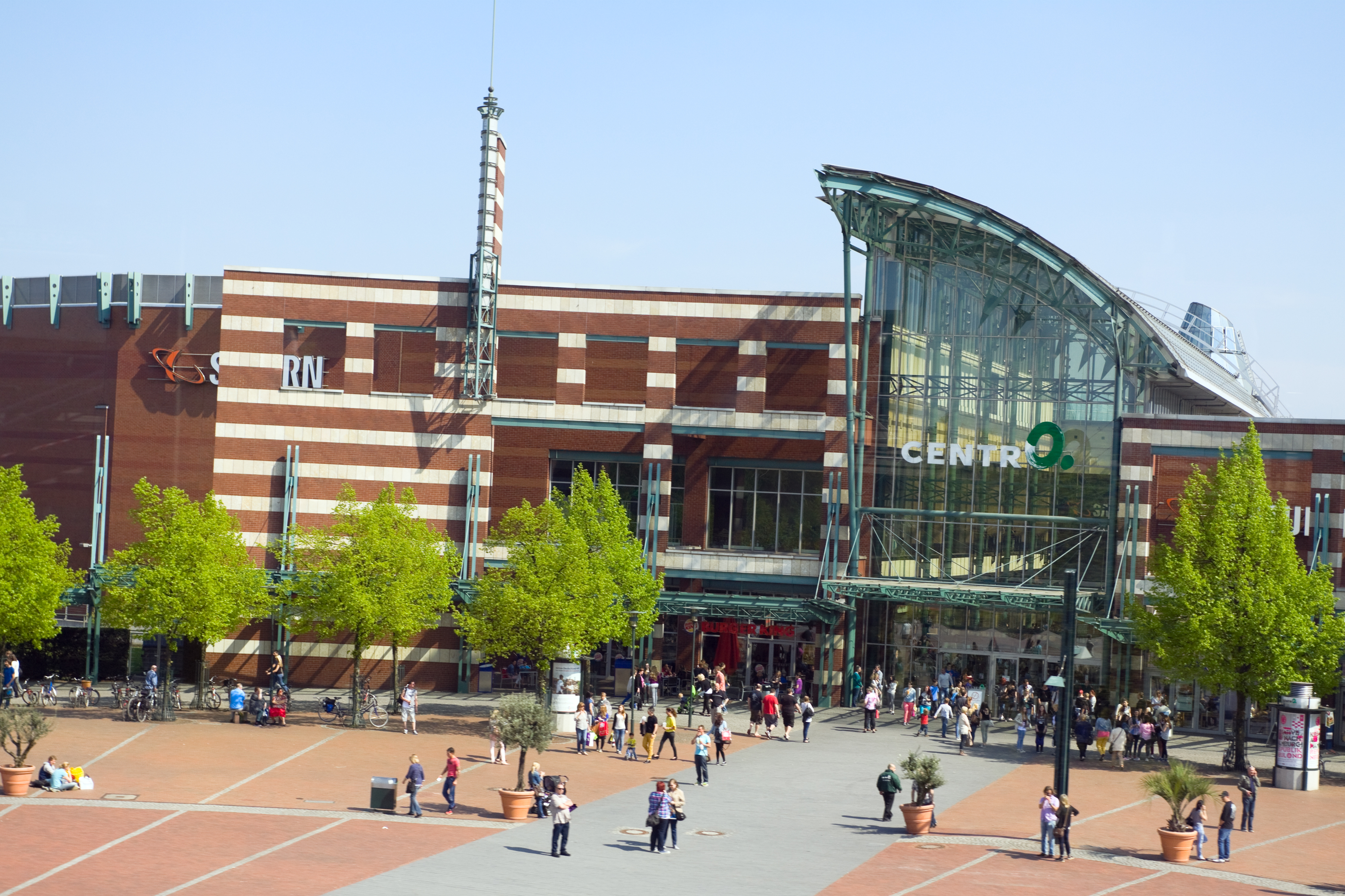 Glass and brick Centro shopping mall, bustling plaza with people and trees.