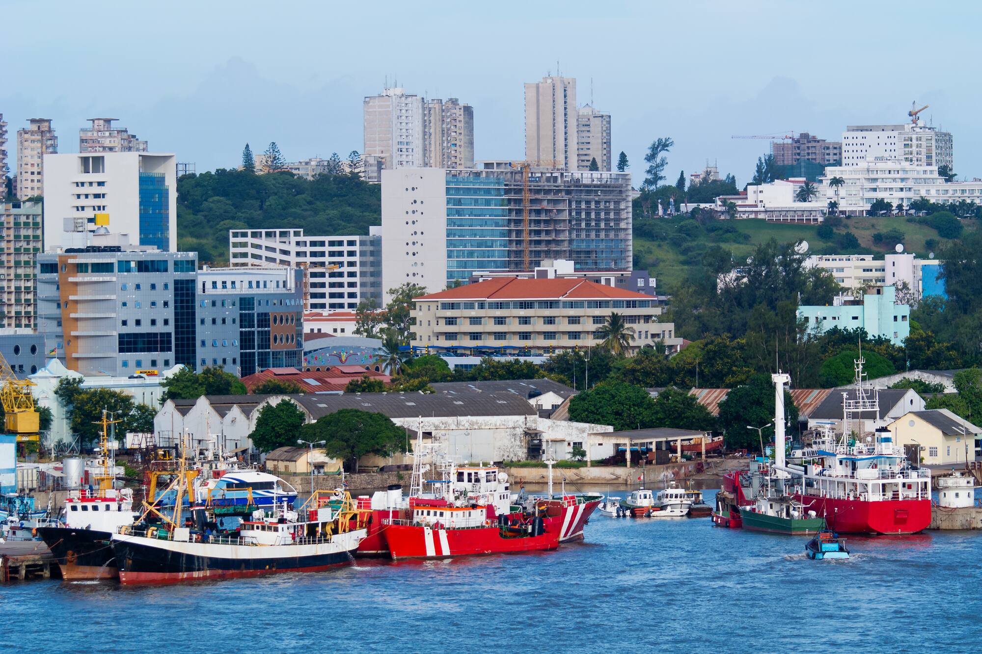 Harbor with fishing boats, modern city buildings, and green hills.