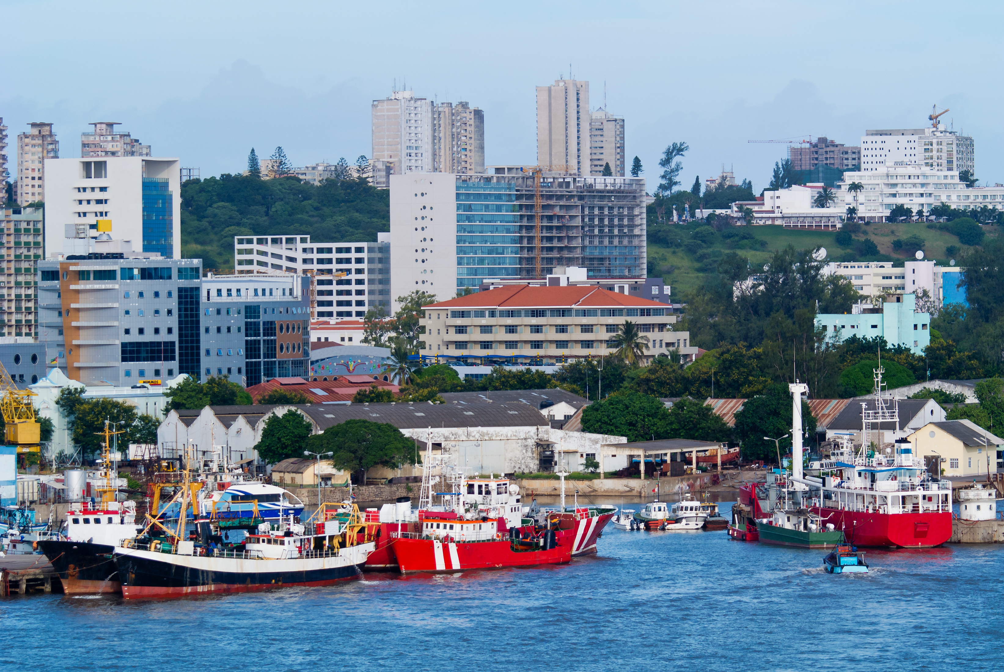 Harbor with fishing boats, modern city buildings, and green hills.