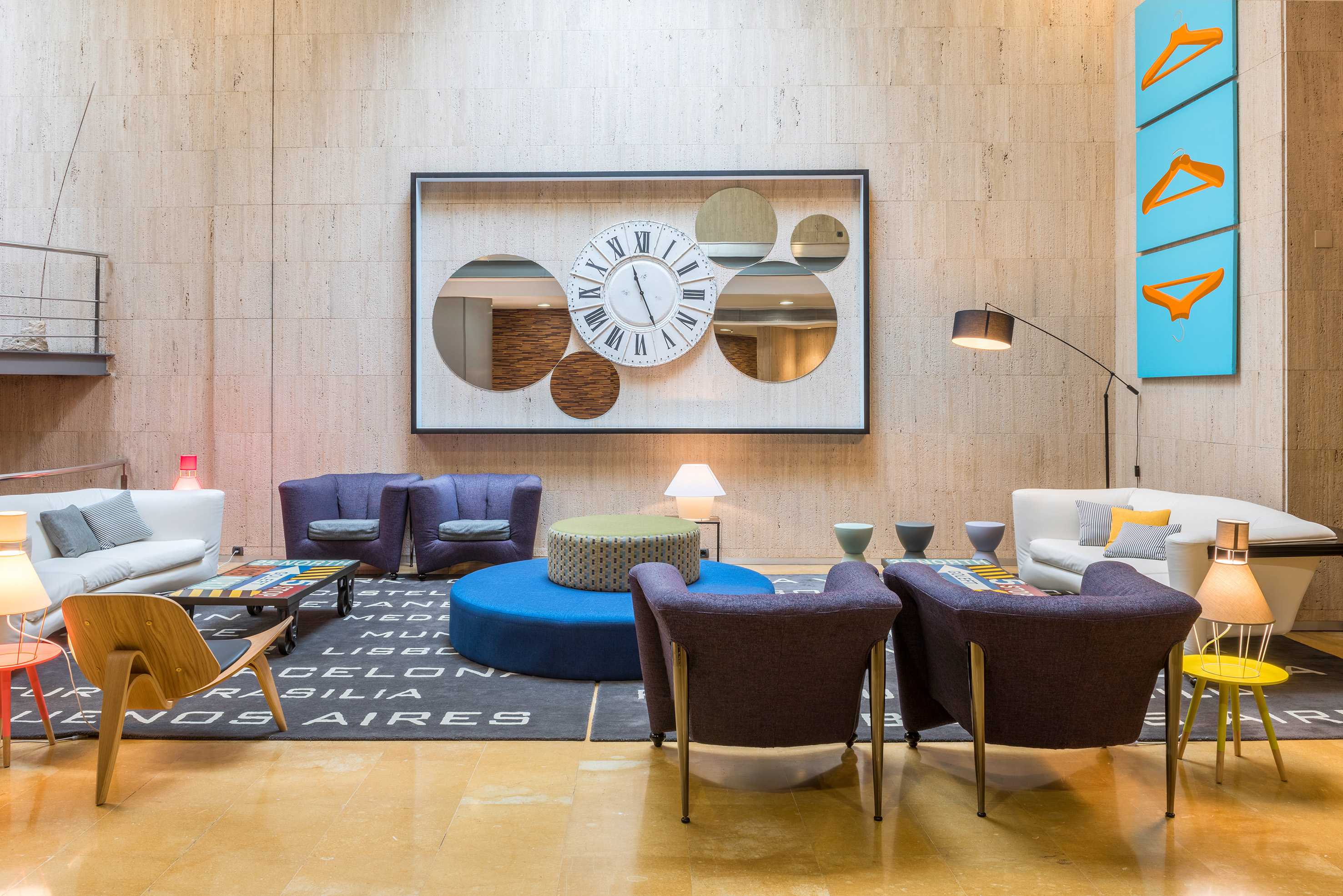 Modern hotel lobby with diverse seating, large clock-mirror decor, and vibrant art.