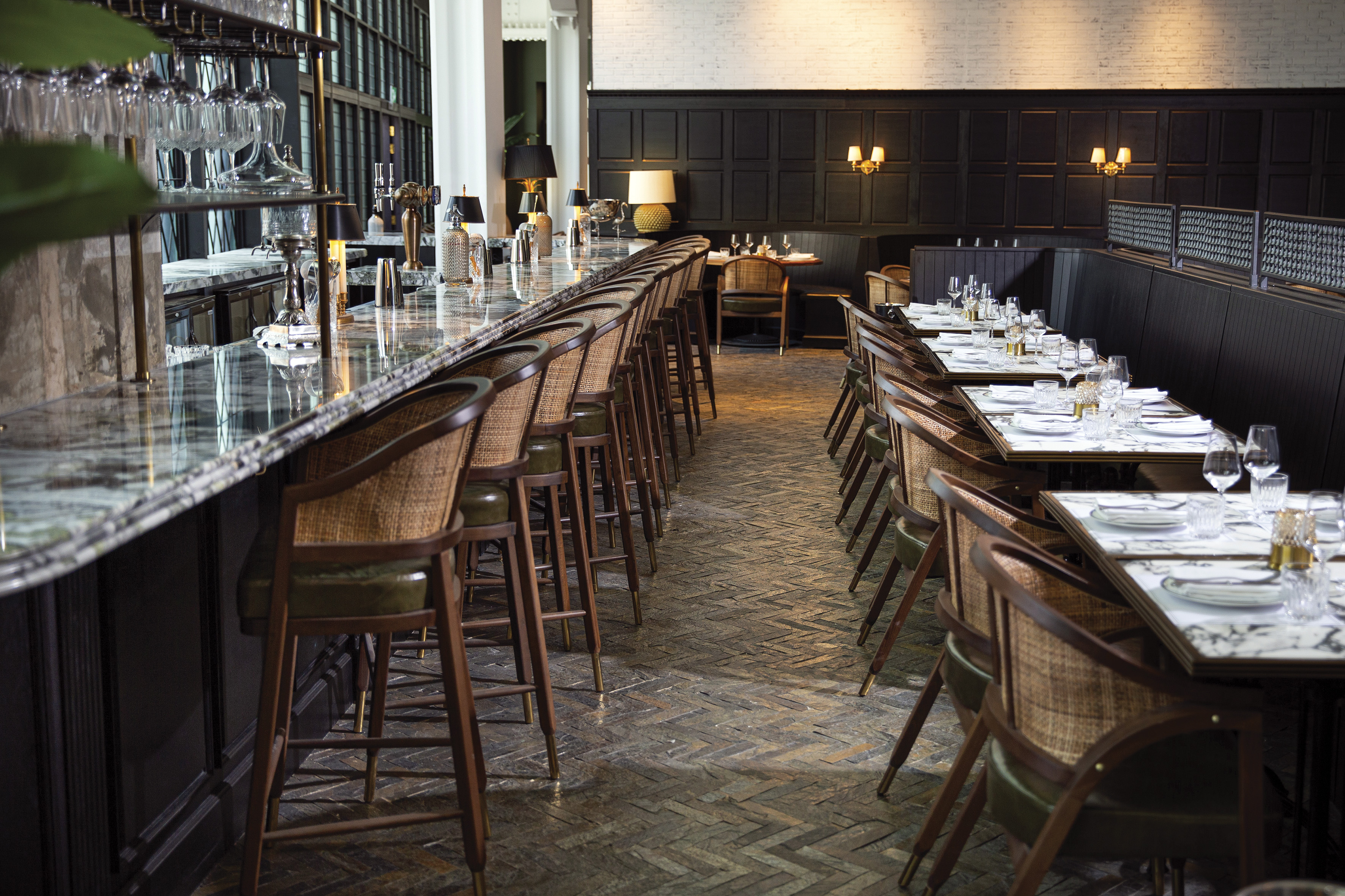 Elegant restaurant bar with marble counter, rattan stools, and set dining tables.