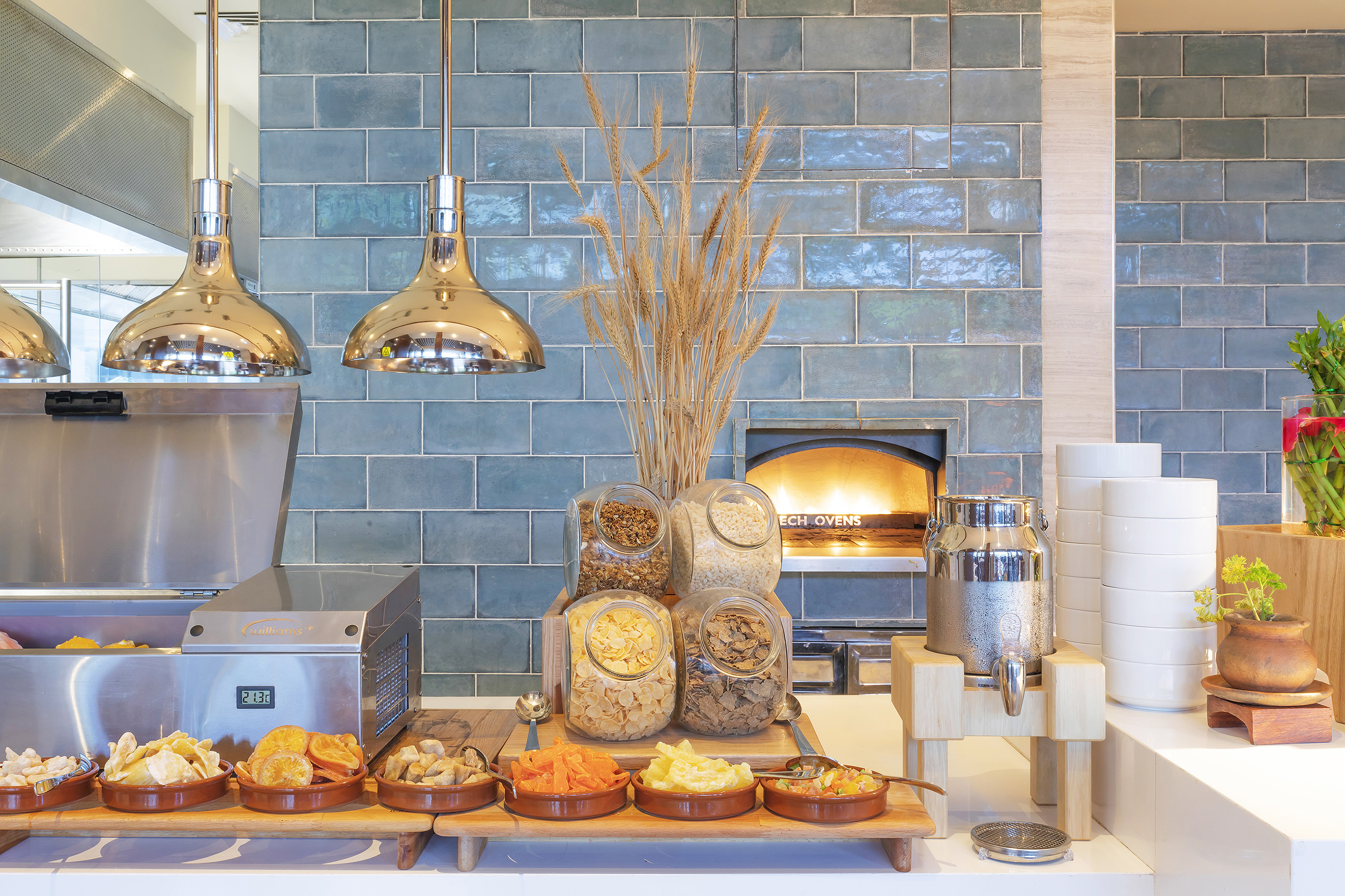 Self-serve breakfast buffet with cereals, dried fruits, dispenser, and blue tiles.