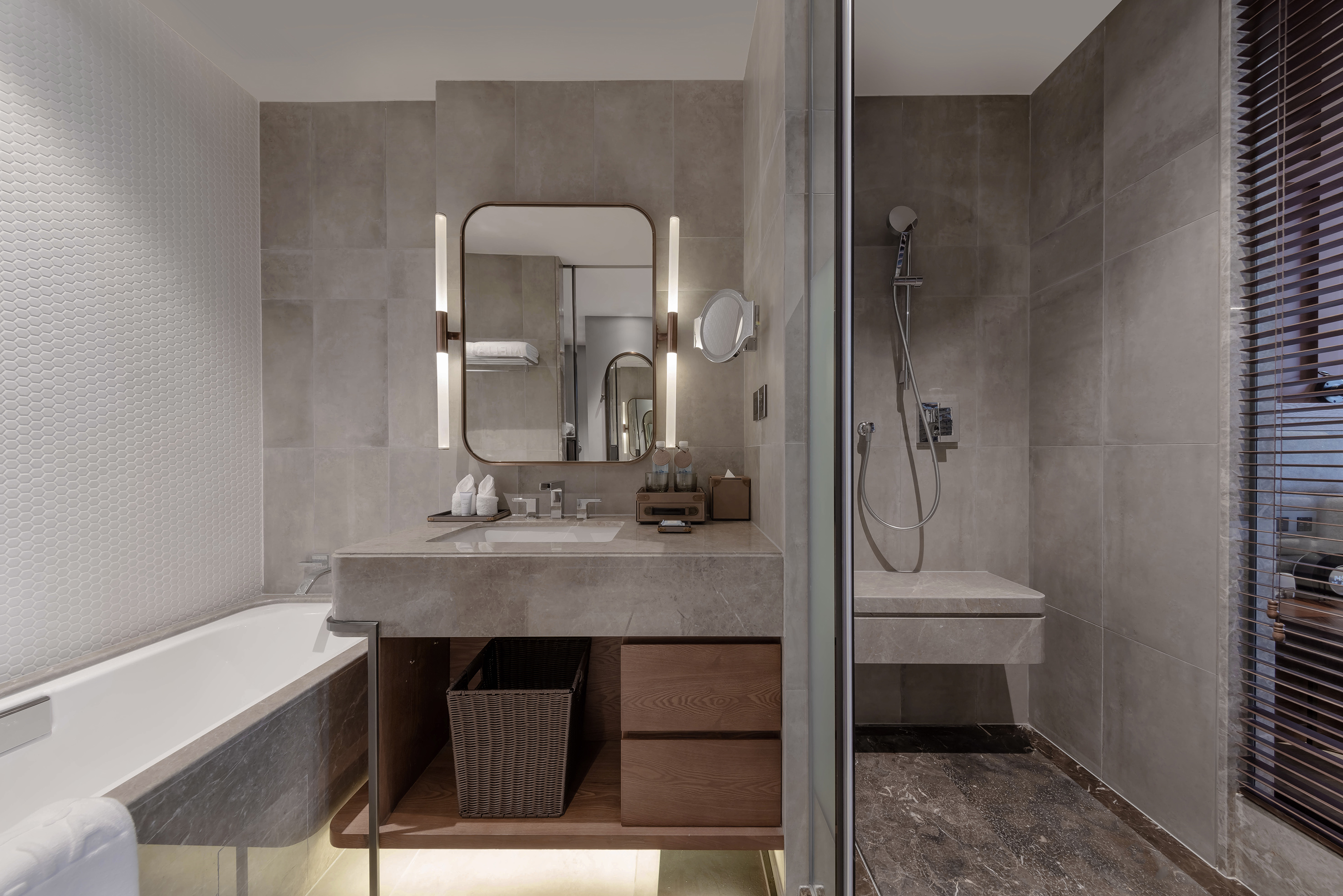 Modern hotel bathroom: gray vanity, illuminated mirror, bathtub, glass shower.