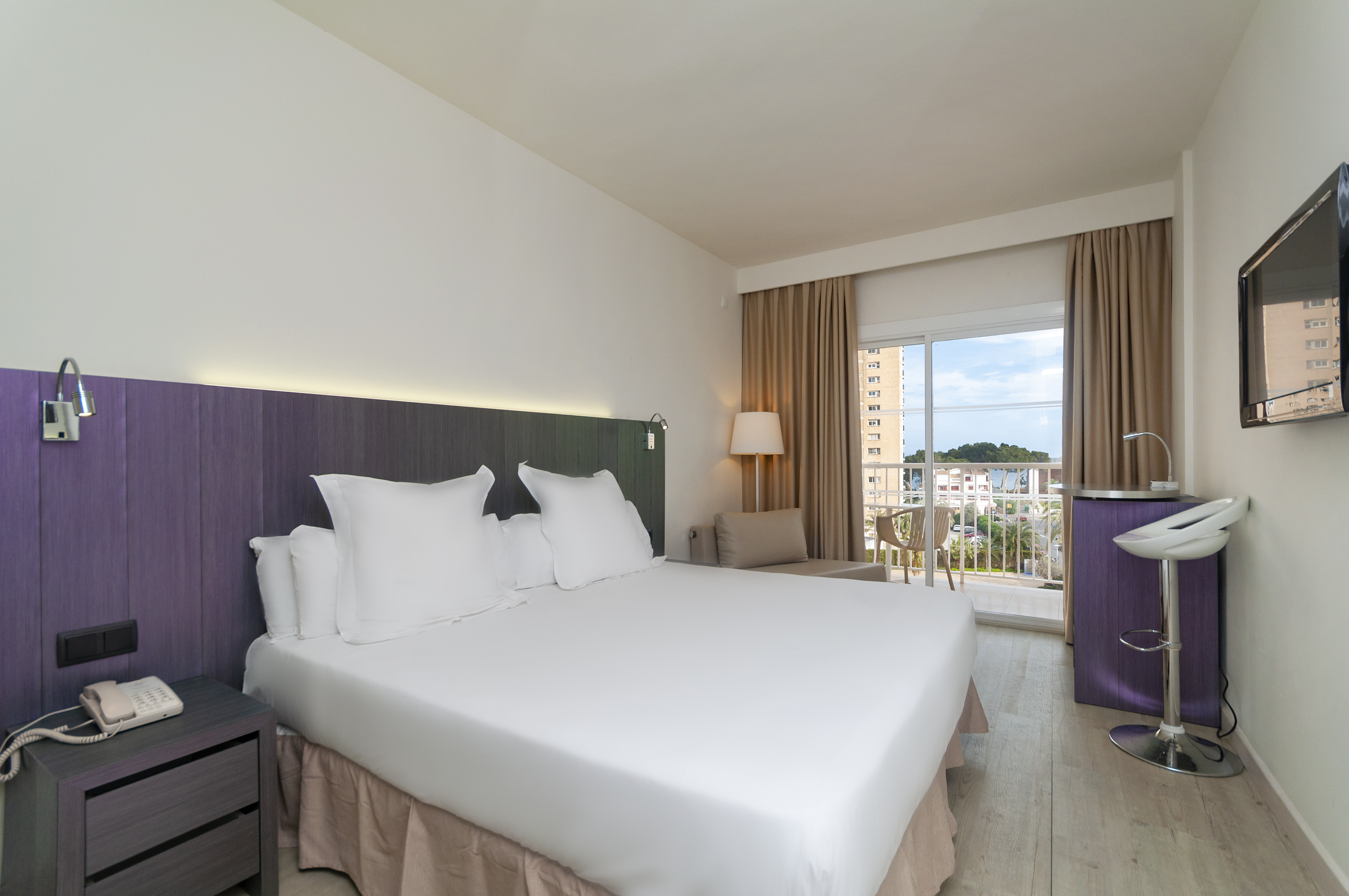 Modern hotel bedroom with white bed, purple headboard, and balcony view.
