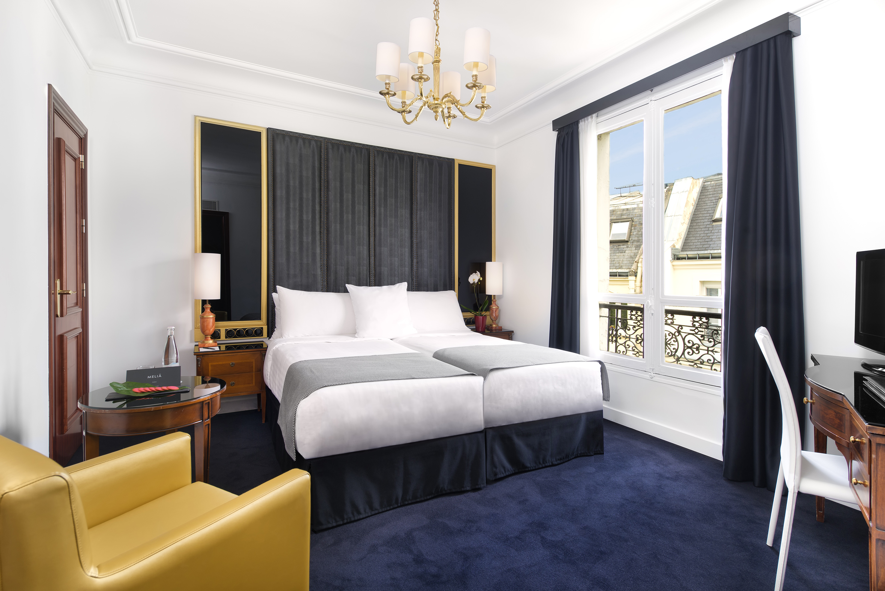 Parisian hotel room with twin beds, blue carpet, and city view.