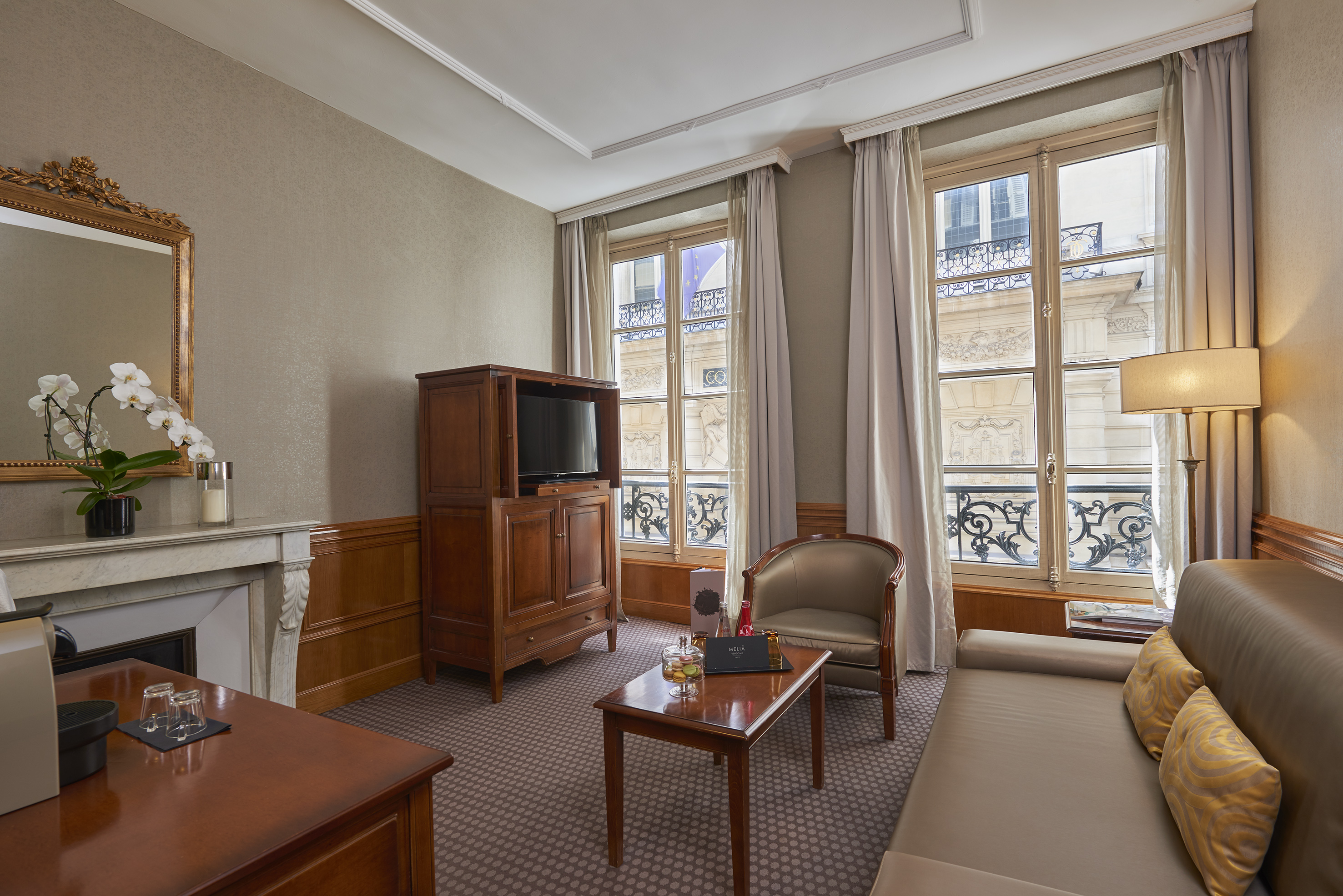 Elegant Parisian hotel suite living room with sofa, TV, and ornate windows.