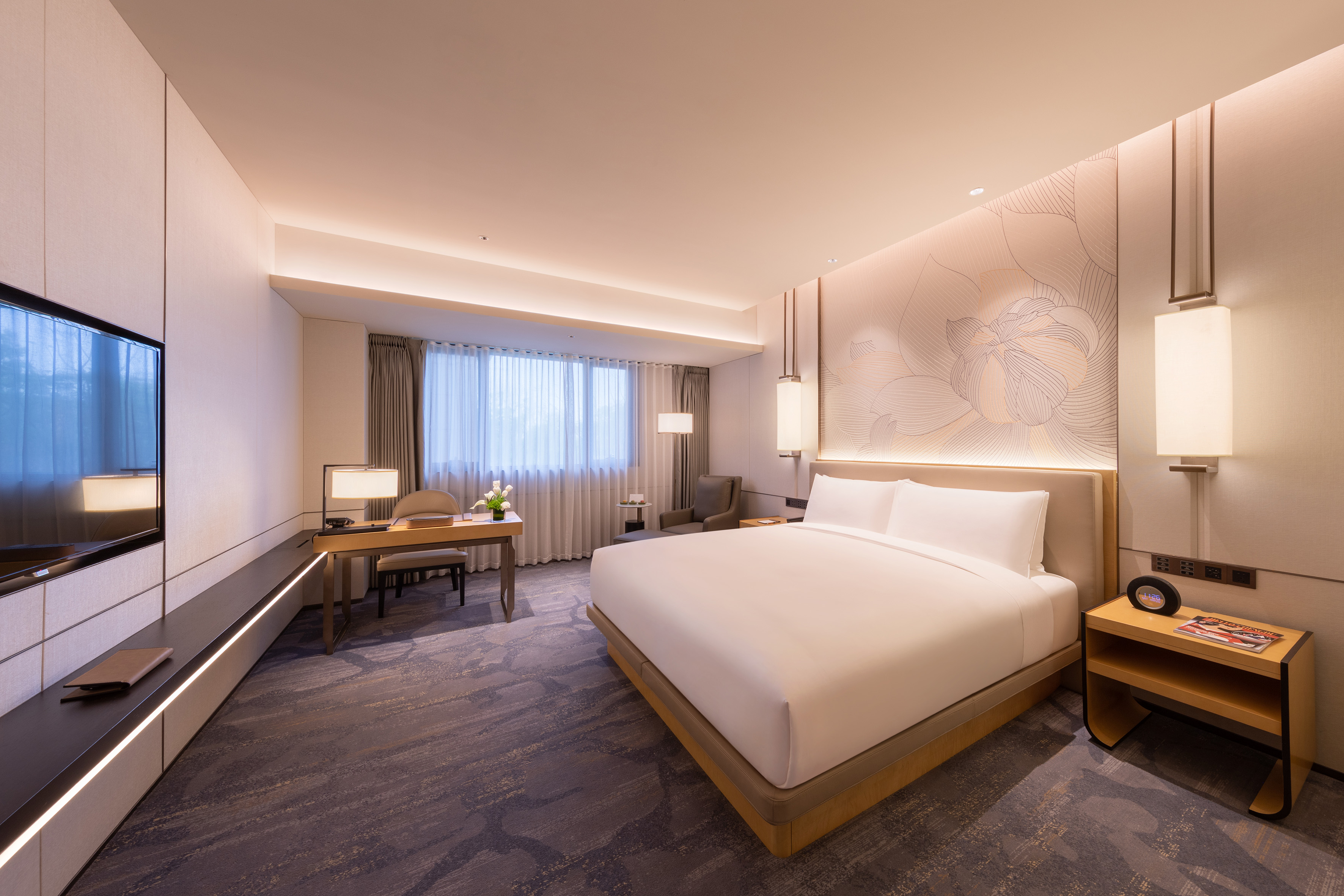 Modern hotel room with large bed, workstation, TV, and contemporary interior design.