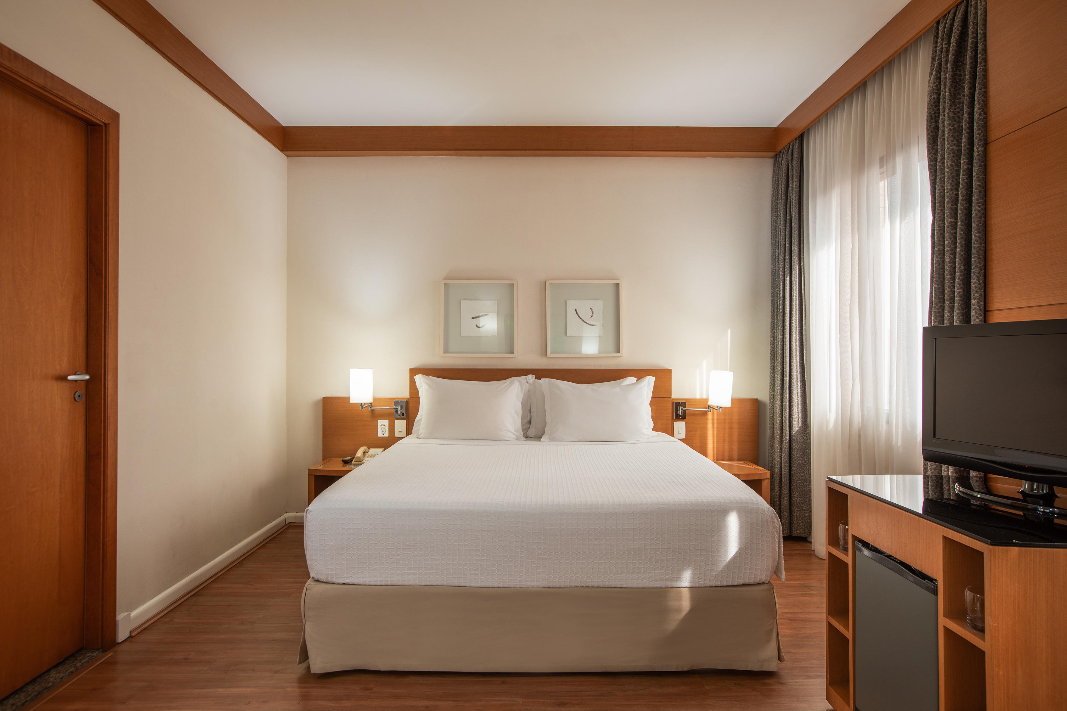 Clean hotel room with king bed, bedside lamps, hardwood floors, and TV.