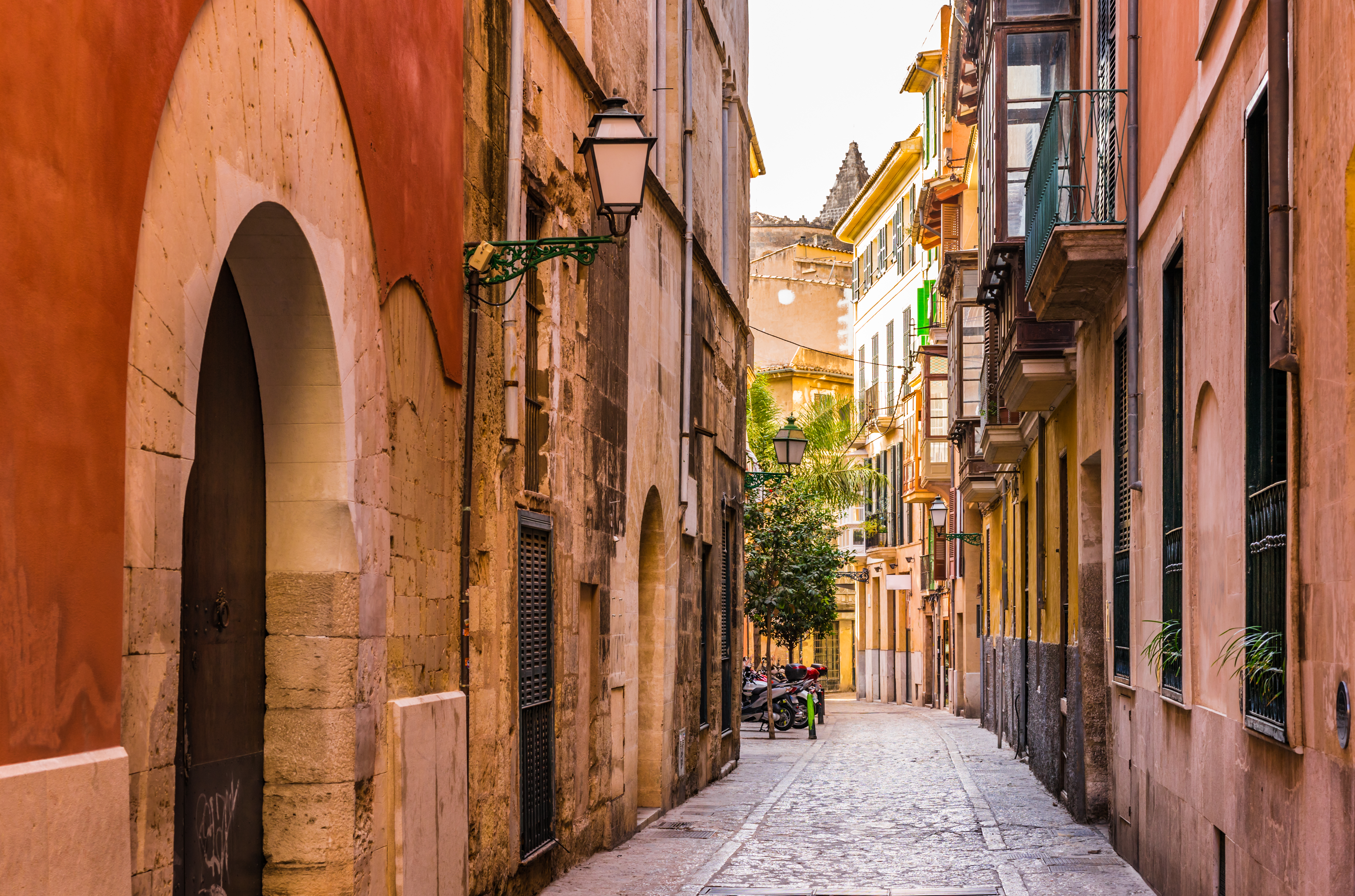 Narrow cobblestone street through a colorful Mediterranean old town, archway, lanterns.
