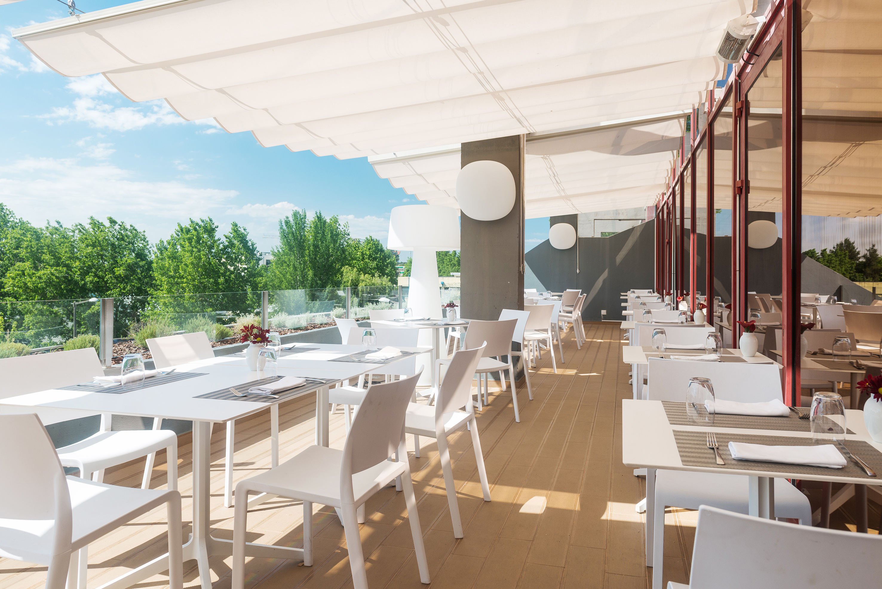 Modern al fresco restaurant terrace with white tables, chairs, and shade canopy.