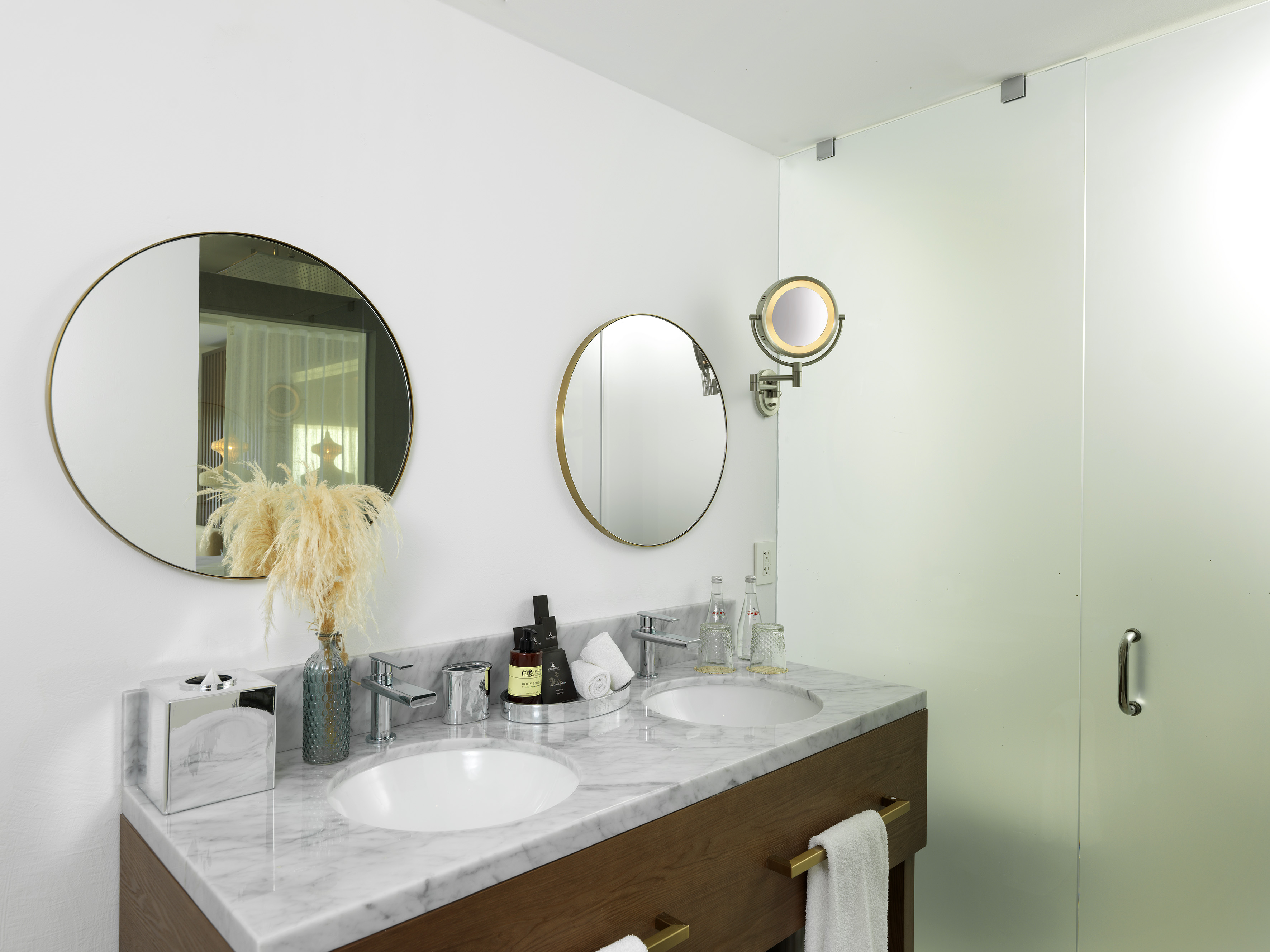 Stylish bathroom with dual sinks, marble vanity, round mirrors, and glass shower.