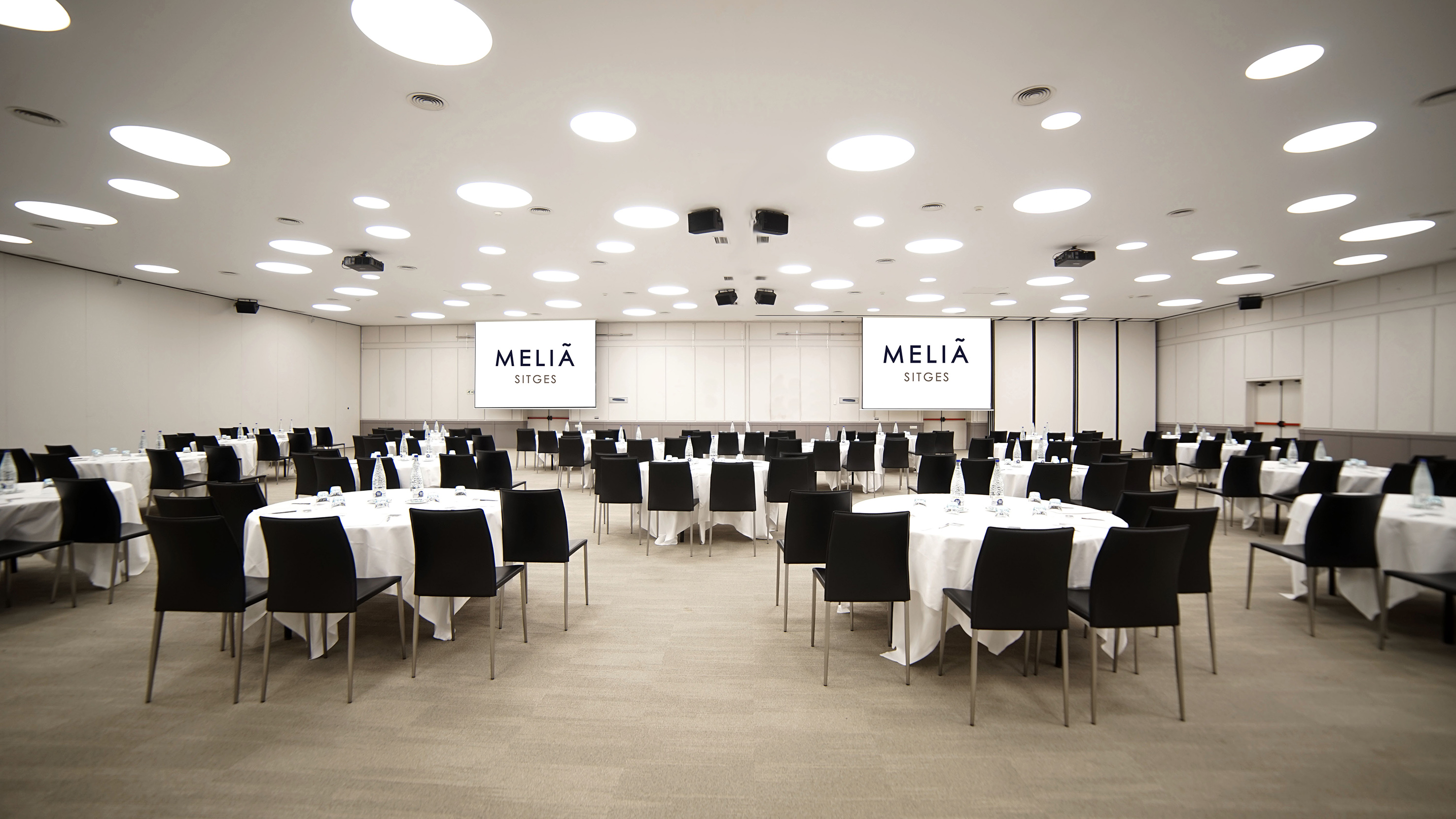 Meliá Sitges conference room with round tables, black chairs, and logo screens.