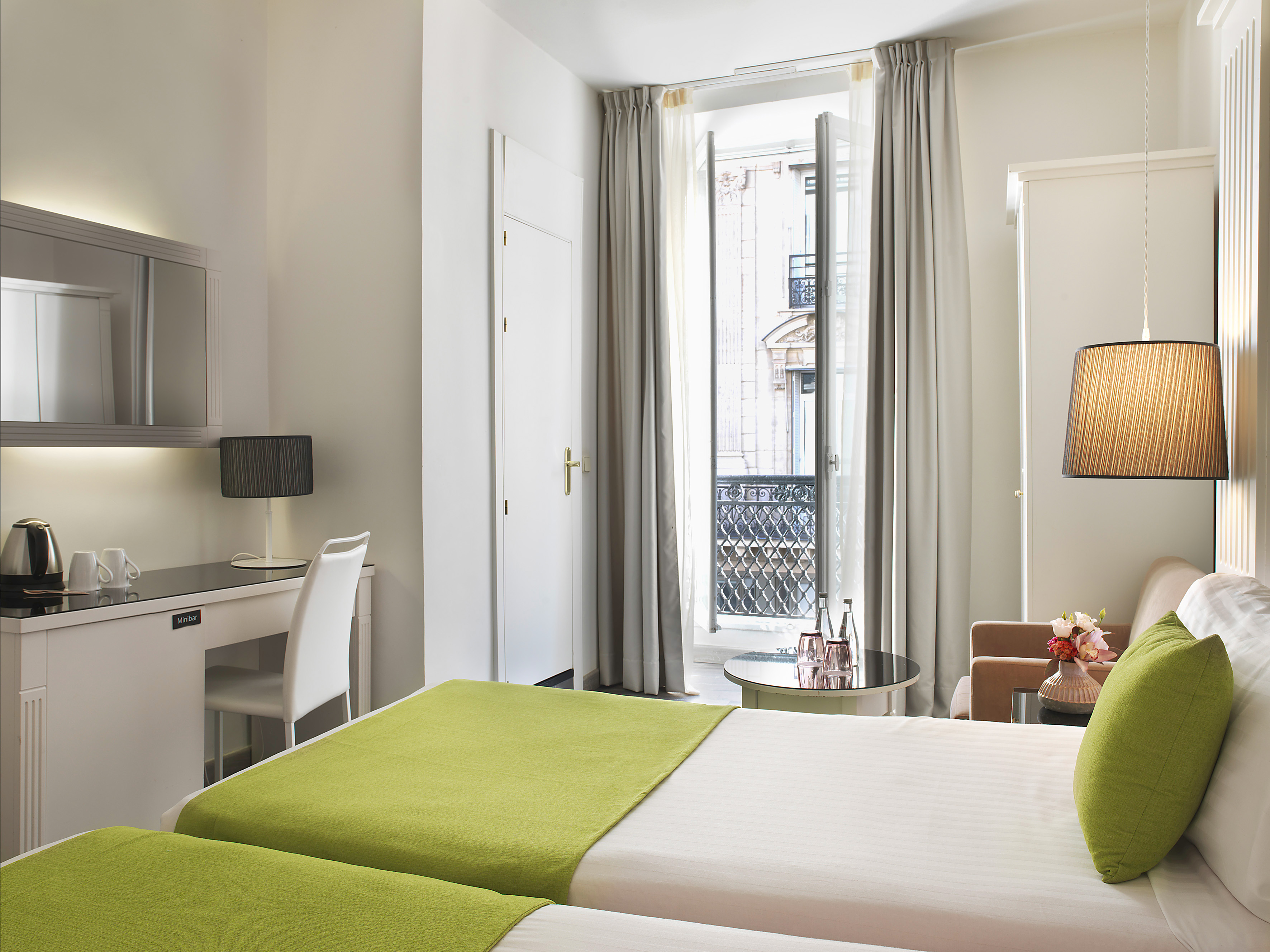 Modern hotel room with twin beds, desk, and open balcony city view.